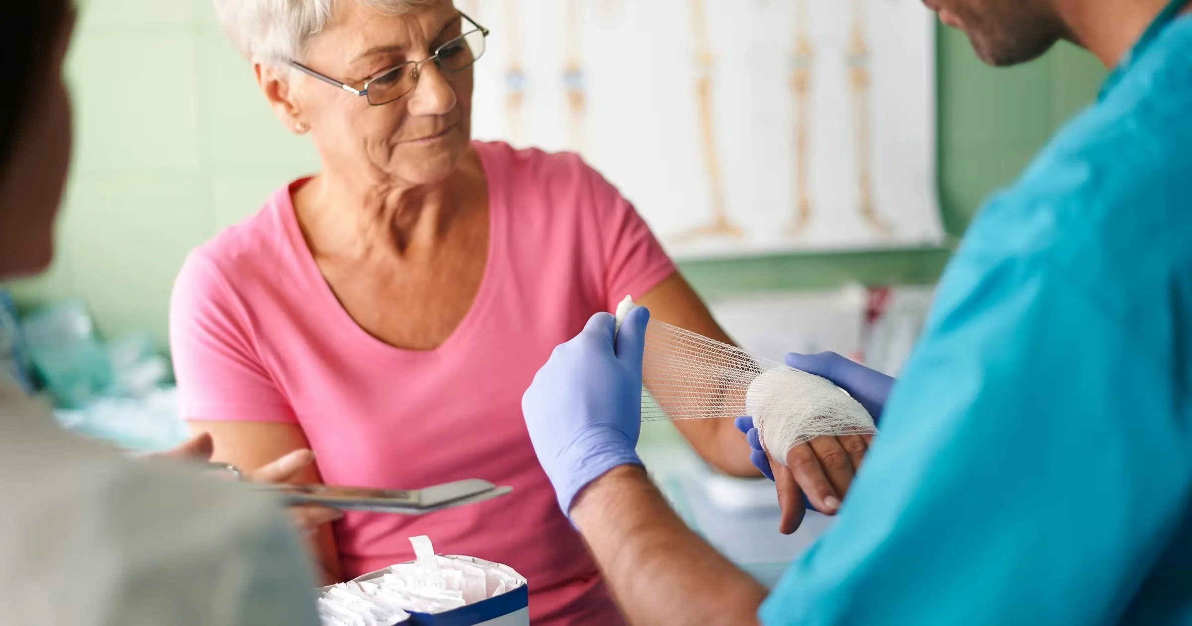 A healthcare worker wrapping a woman's hand with a bandage in a medical setting.