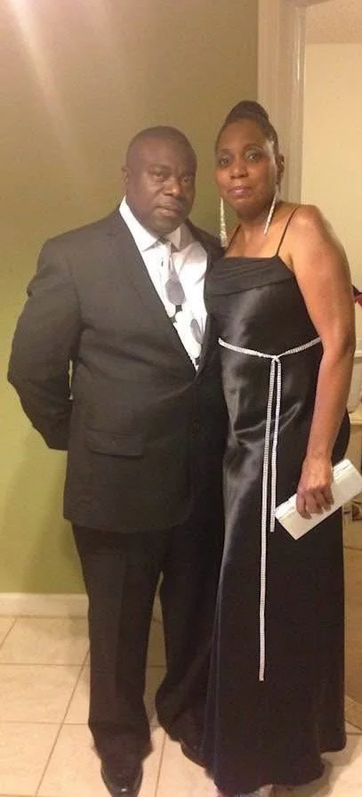 A man and woman dressed in formal attire standing together inside a room with beige walls and tiled floor.
