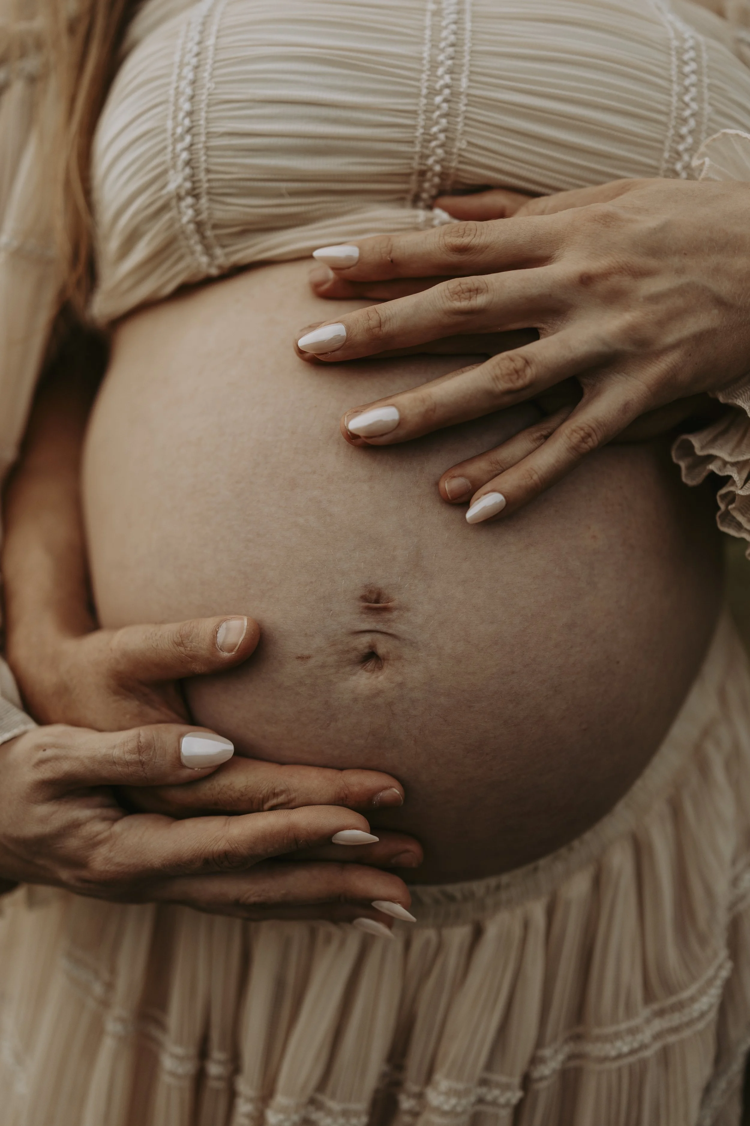 Close-up of a pregnant woman's belly being gently held by several hands.