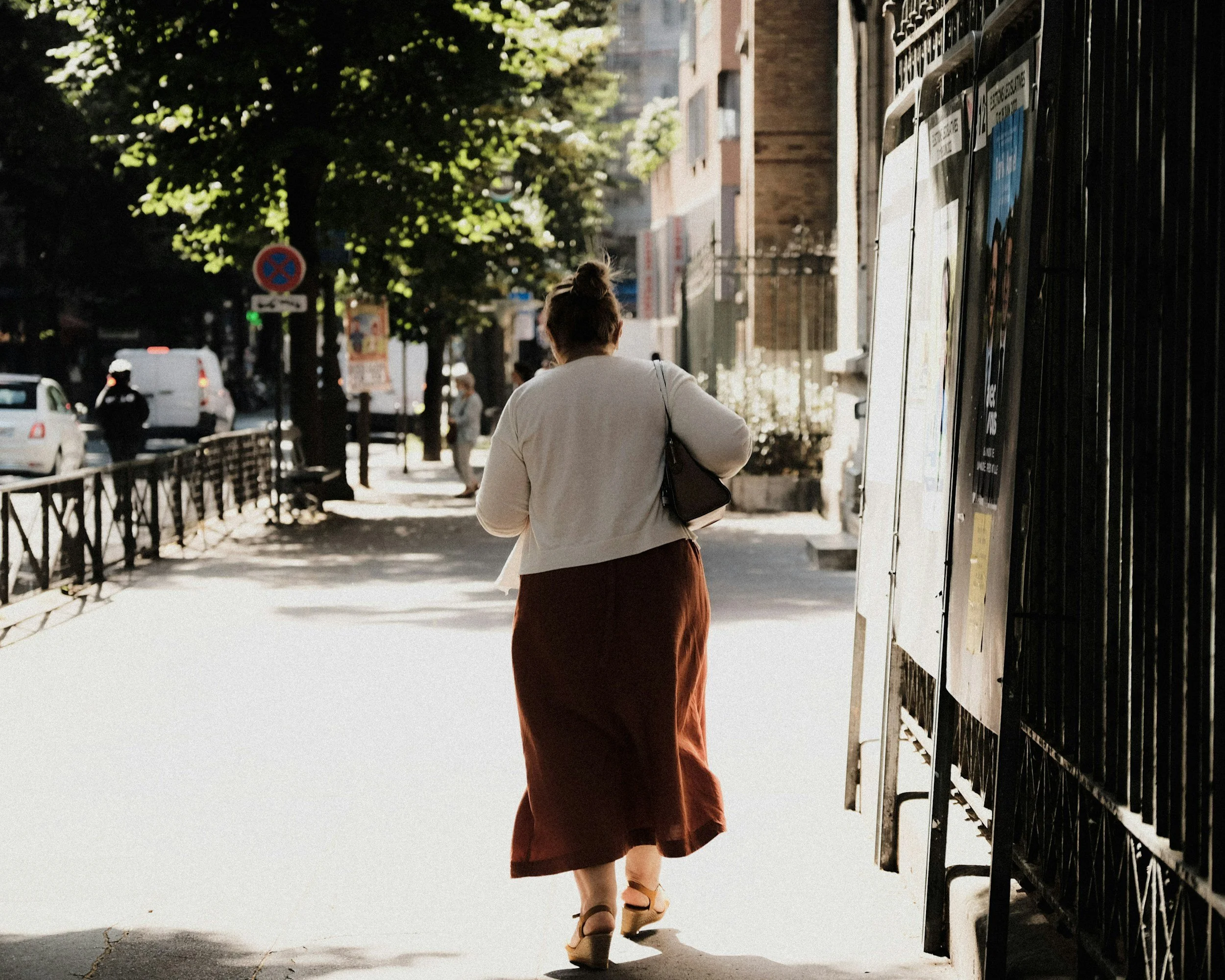 Woman walking along a sunlit tree-lined sidewalk