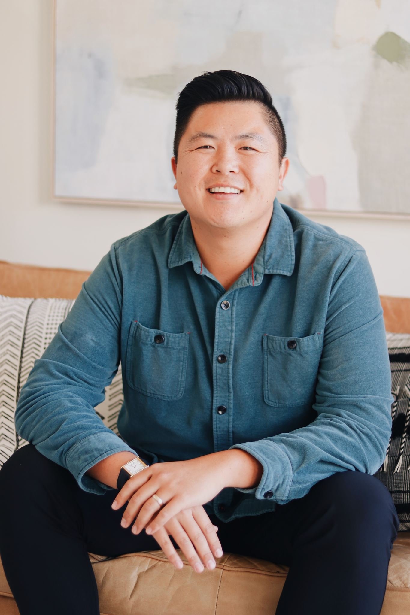 Man with dark hair wearing green button down shirt sitting on a couch