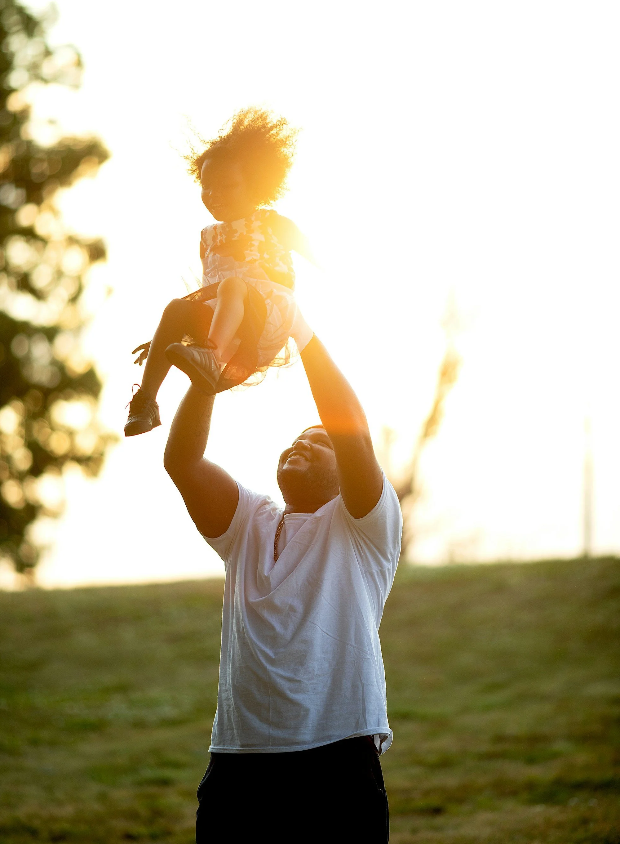 A father lifting his child into the air at sunset, both backlit by golden light.