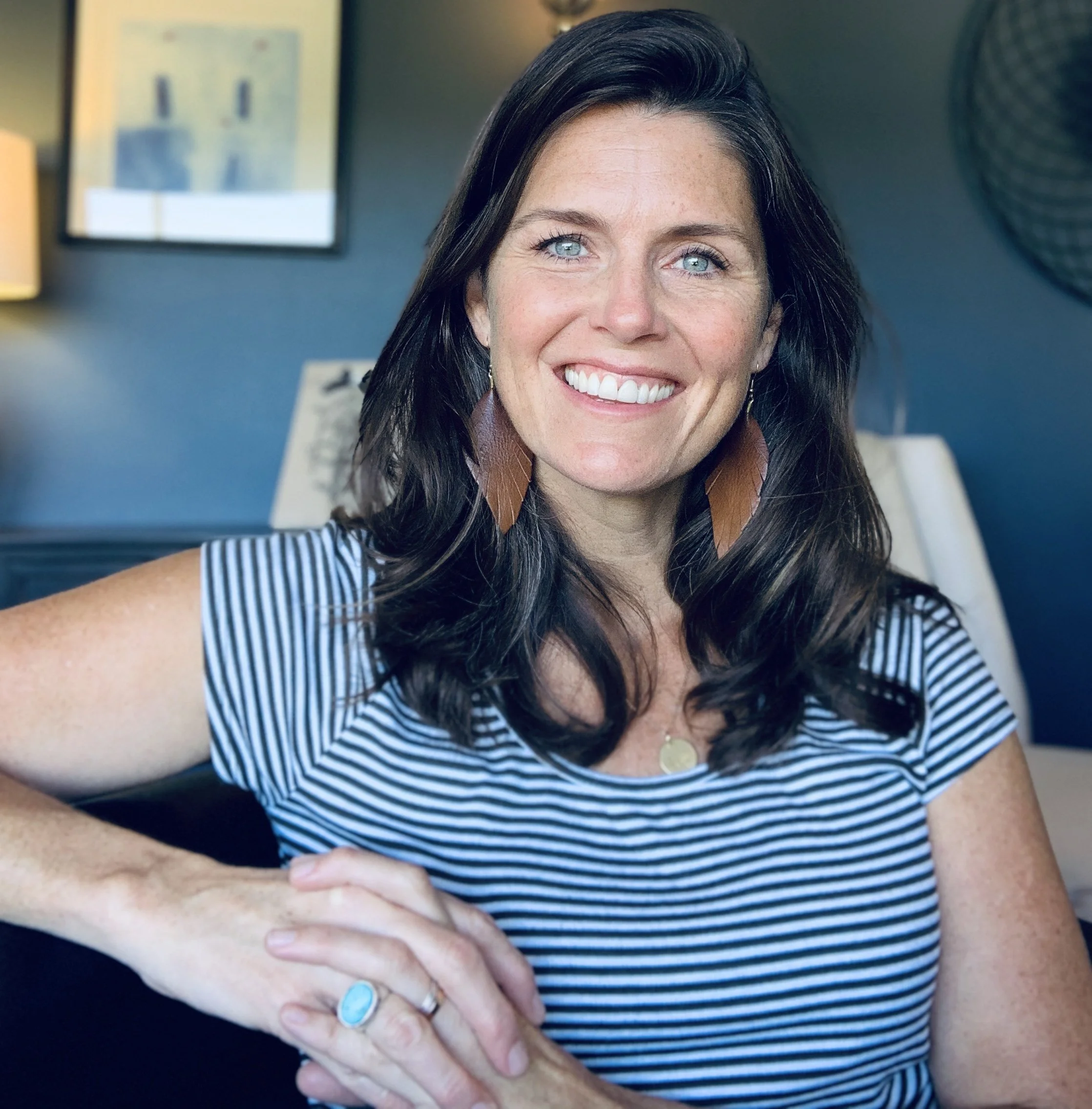 Melanie Wolf, therapist in San Diego. A woman with long dark hair and blue eyes smiling at the camera, wearing a striped shirt, large earrings, and a ring.