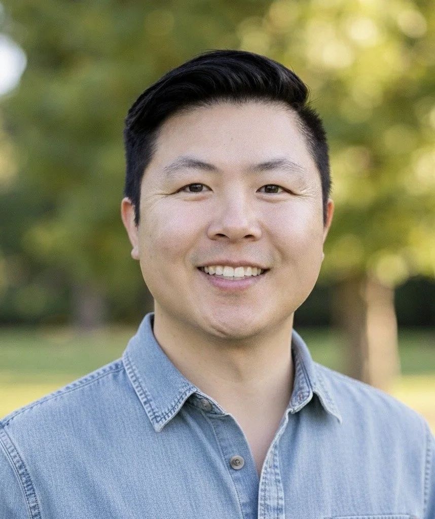 Brandon Wong, therapist in San Diego. A smiling man with black hair wearing a light blue button-up shirt outdoors with a blurred background of greenery.
