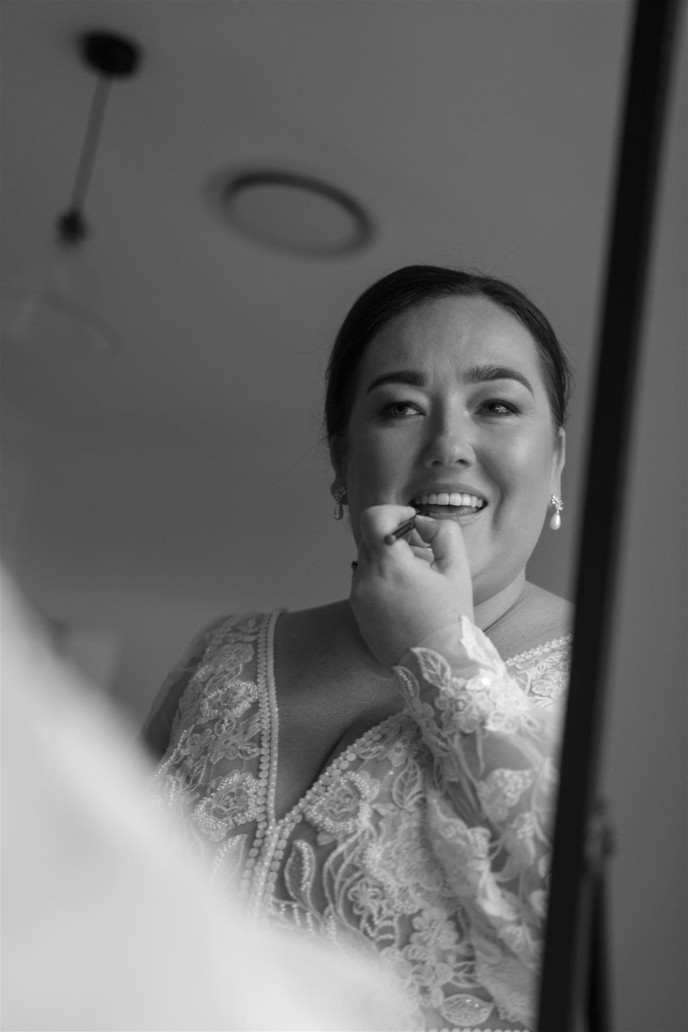 A woman in a lace dress looks into a mirror while applying makeup.
