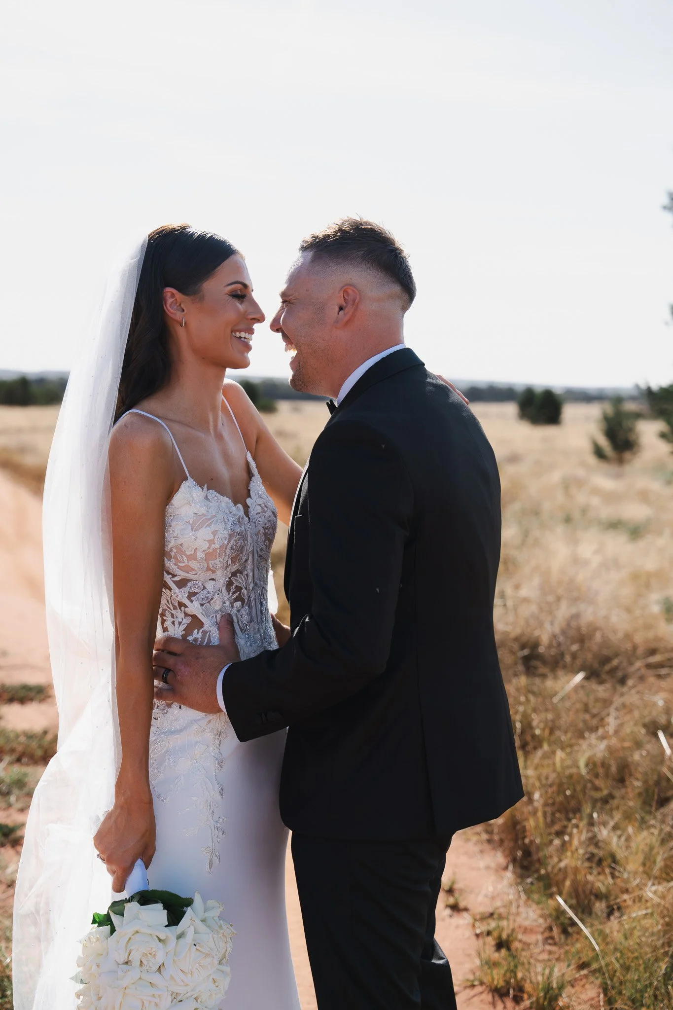 A bride and groom smiling and looking at each other in a field during their wedding.