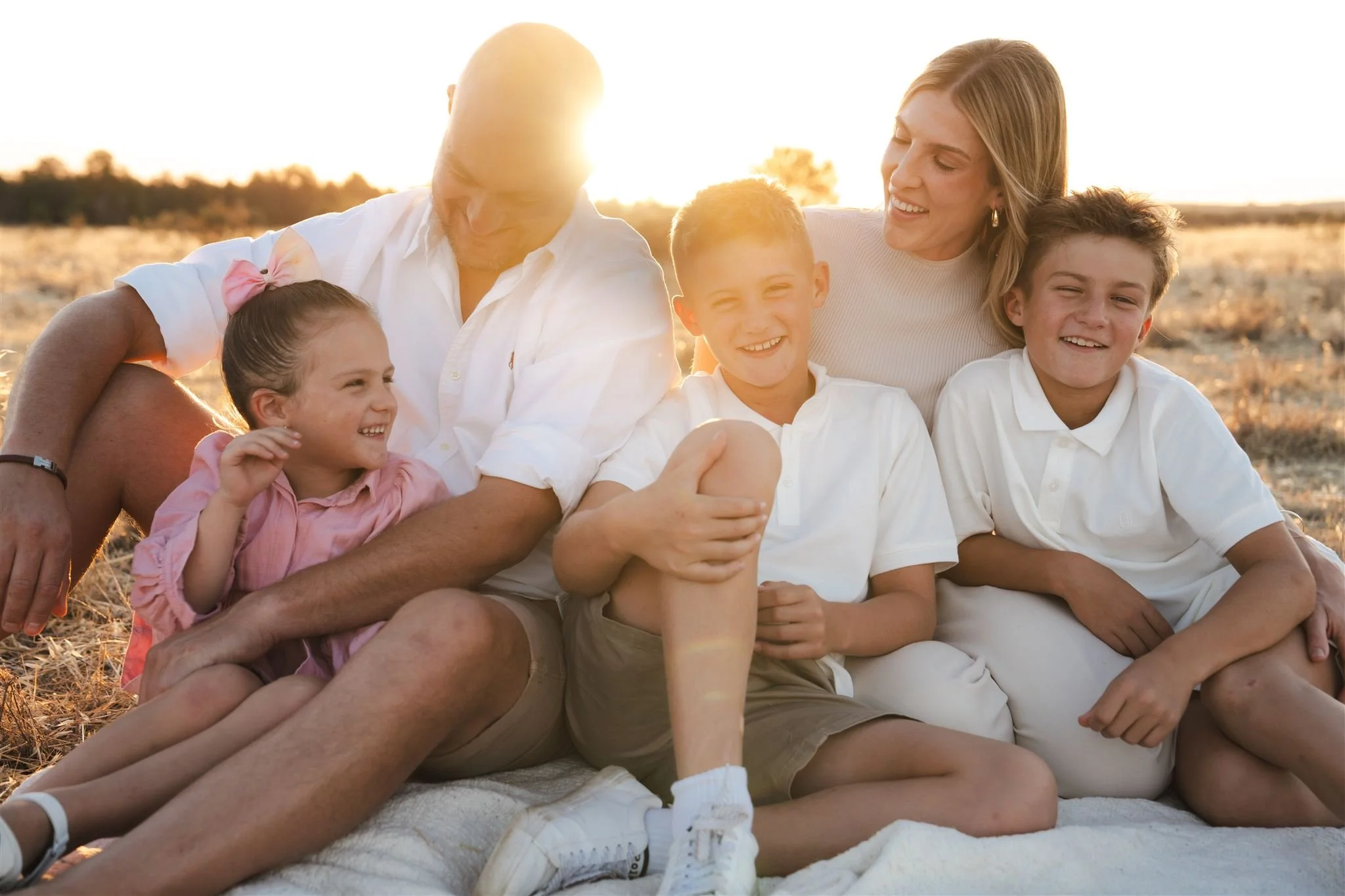 family session, sunset, A happy multigenerational family of two adults and three children sitting together on a blanket outdoors at sunset.