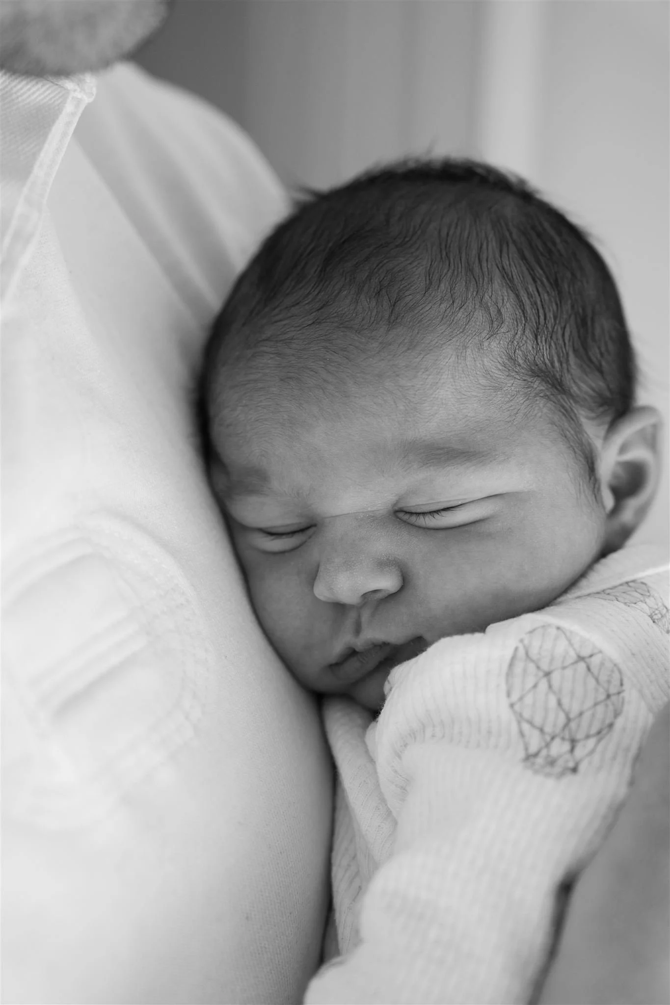 newborn session, Black and white photo of a sleeping baby cradled against an adult's shoulder.