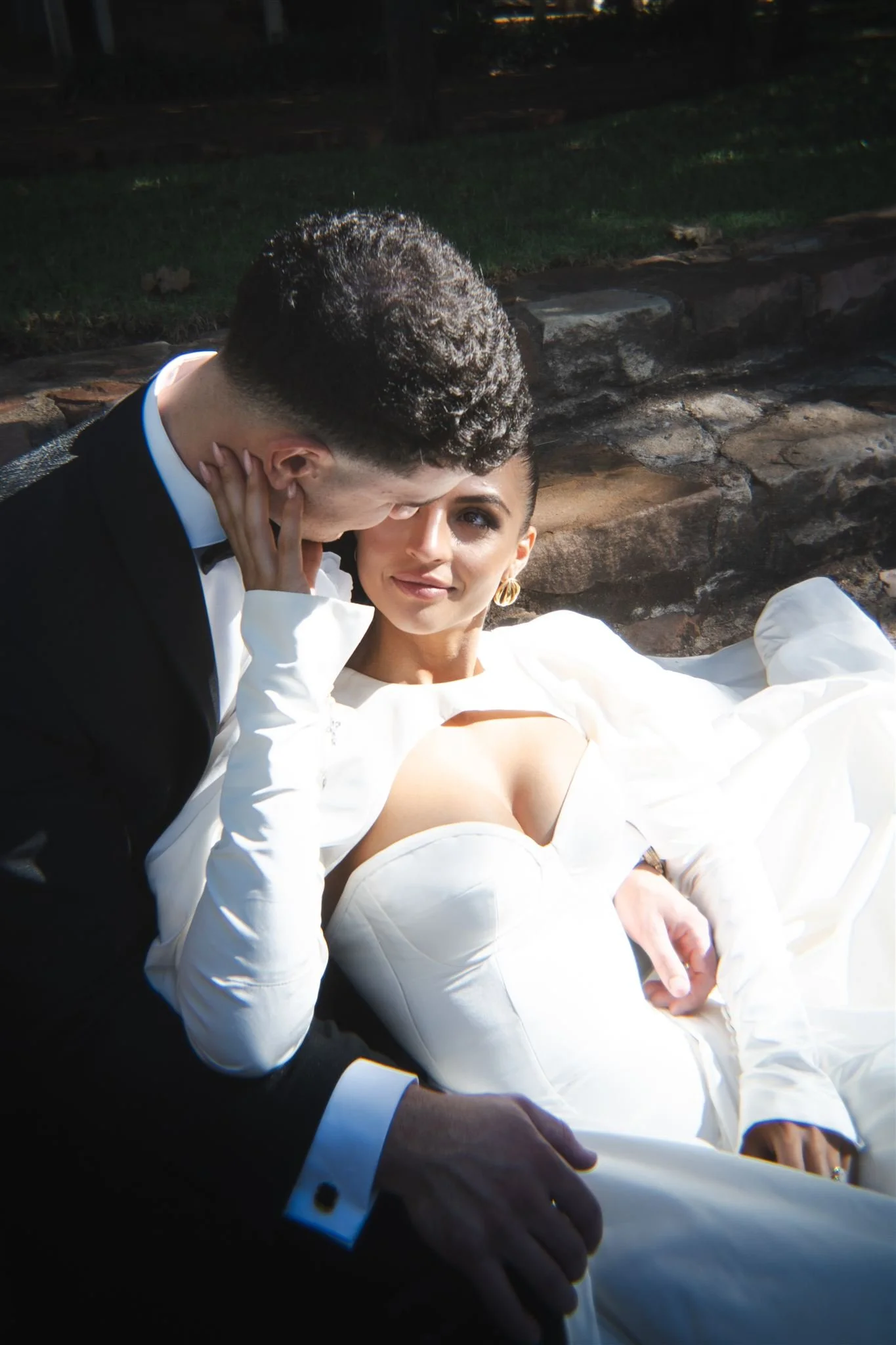 A bride and groom sitting together outdoors at night, with the groom gently holding the bride and leaning in close to her.
