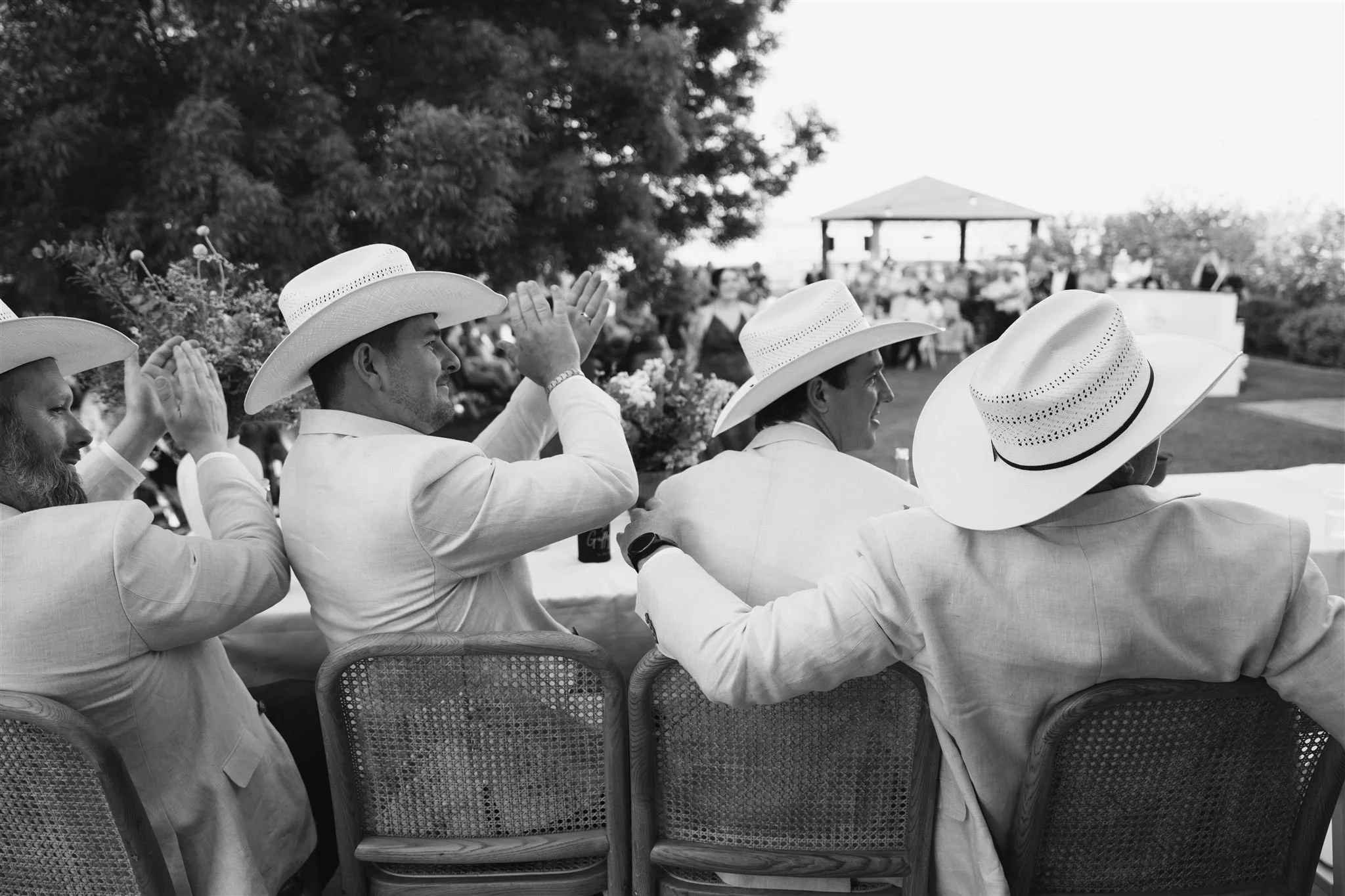 Groomsmen, cowboy wedding, cowboy, cowboy hat, wide-brimmed hats, some raising their hands, in a black-and-white outdoor gathering.