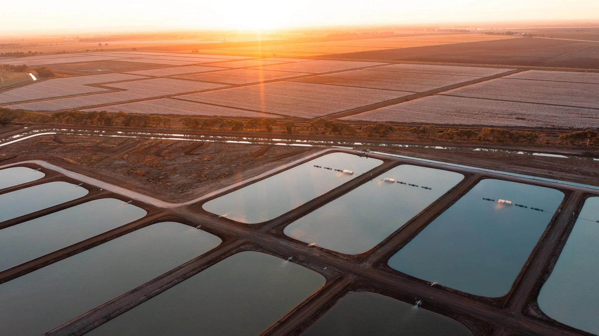 Drone content. Aerial view of a farm with rectangular ponds and fields at sunset, with irrigation equipment and distant fields.