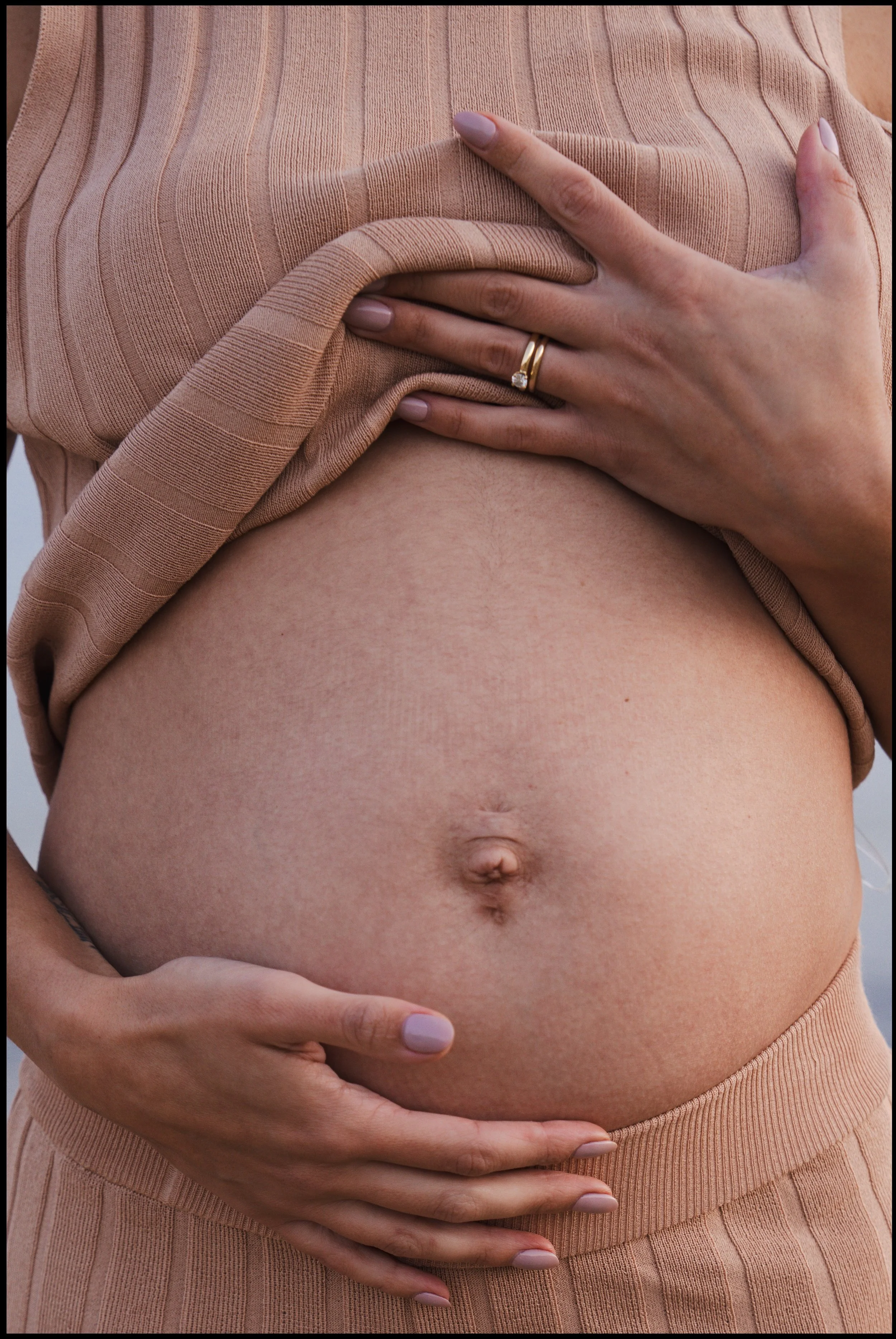 Close-up of a pregnant woman's belly being gently touched by her hands, one hand with a wedding ring.