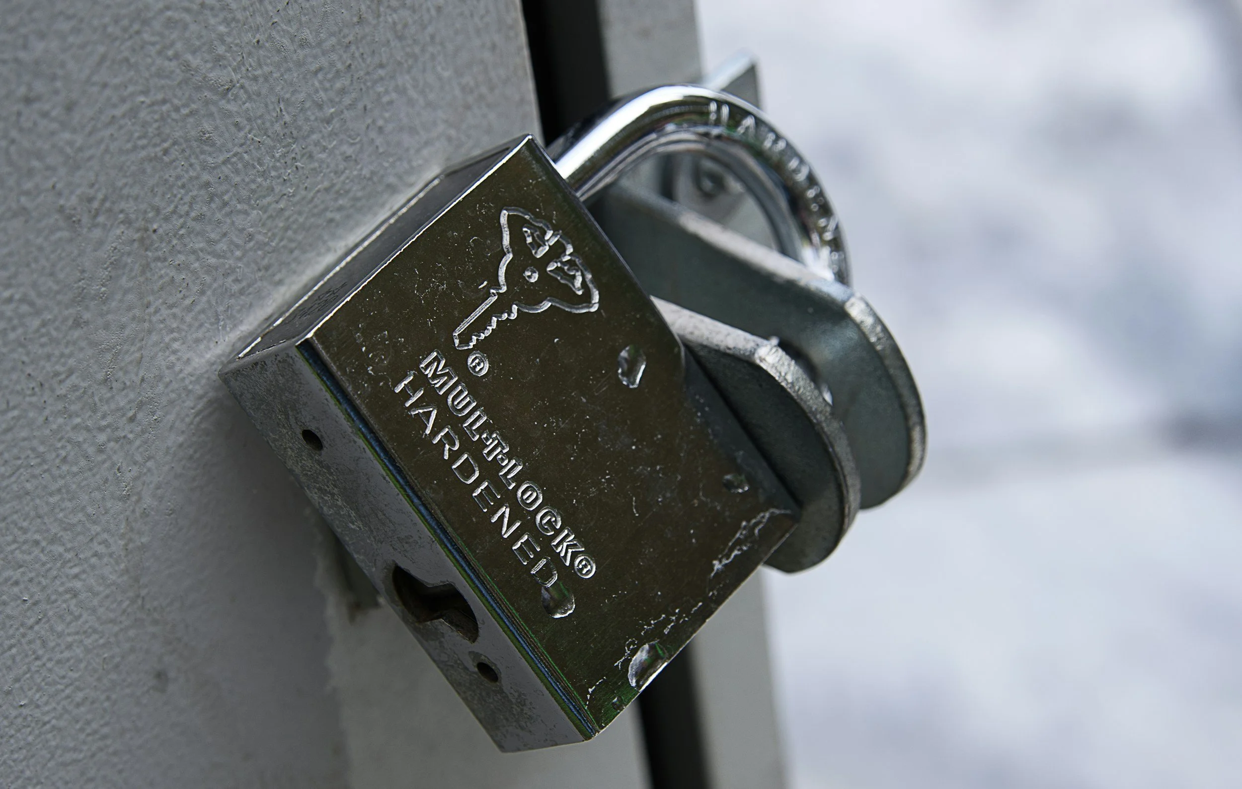 Close-up of a silver padlock attached to a gray textured surface, with some snow visible in the background.