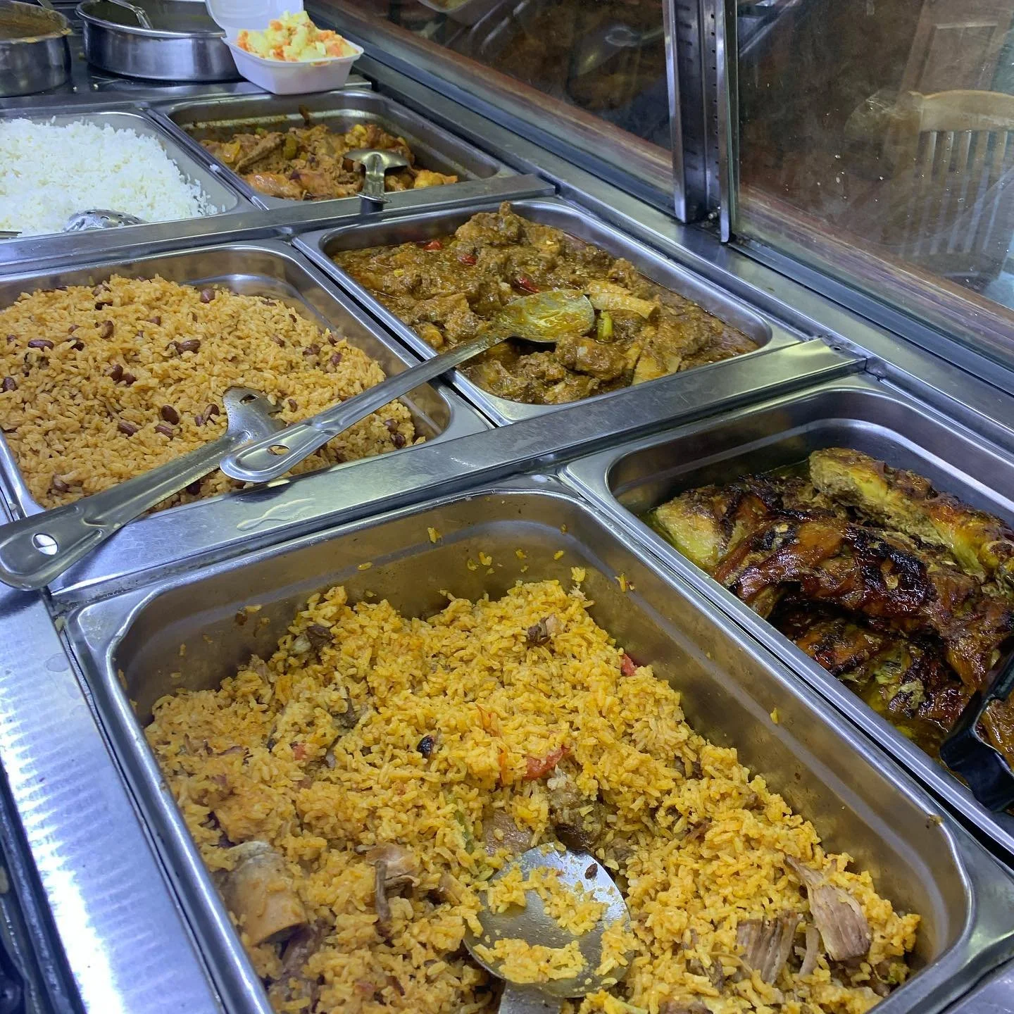 Food buffet with trays of rice, stewed meat, fried chicken, and roasted ribs.