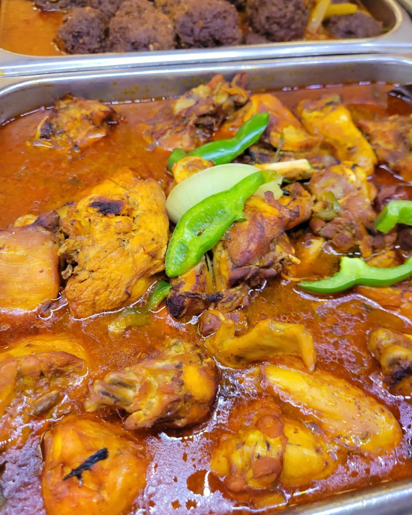 Close-up of a tray of Indian chicken curry with green chili garnishes.