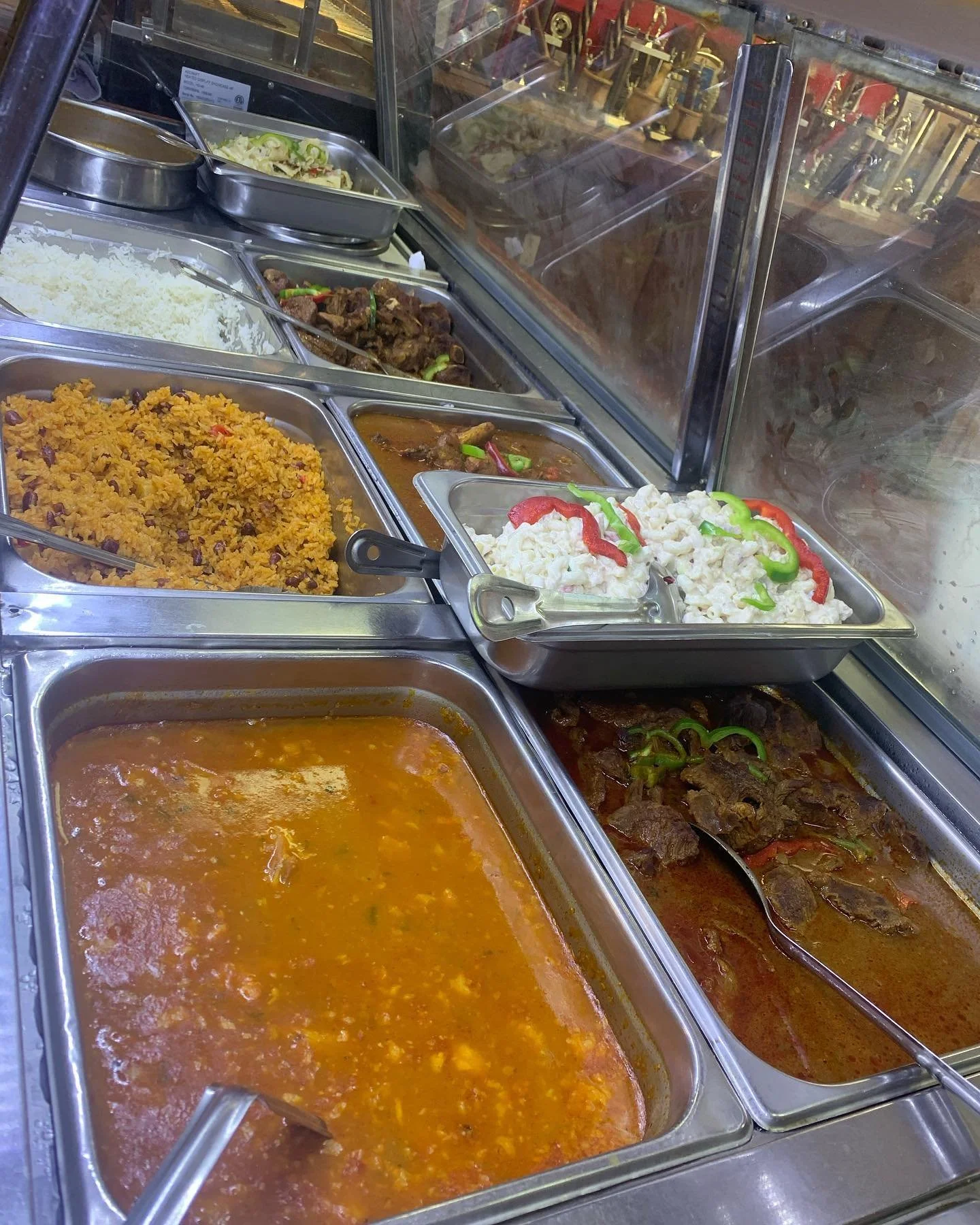 A variety of hot dishes in a buffet, including rice, beef stew, macaroni salad, chili, and cooked beef with vegetables.