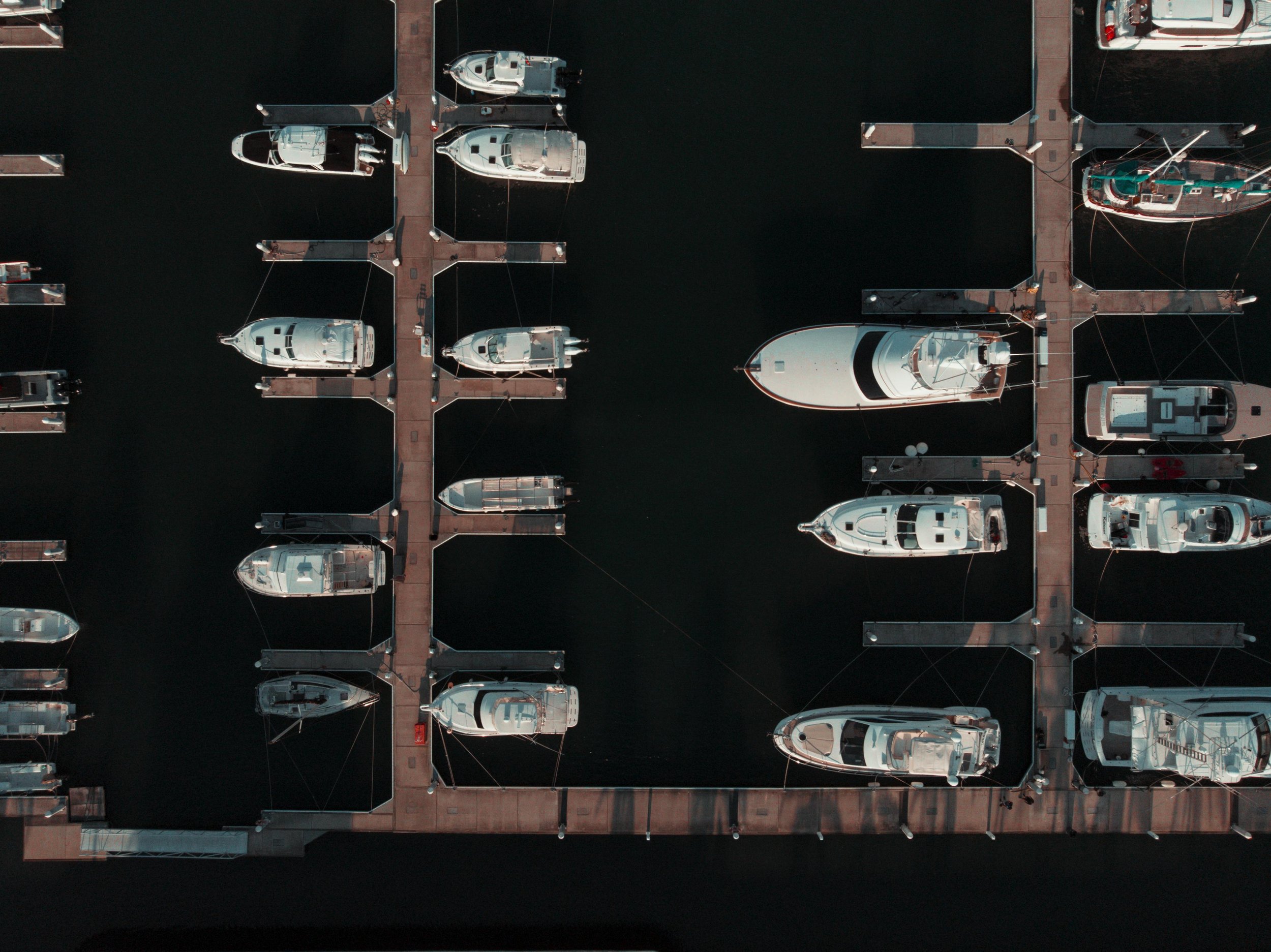 An aerial view of a marina with boats docked along wooden piers on dark water.