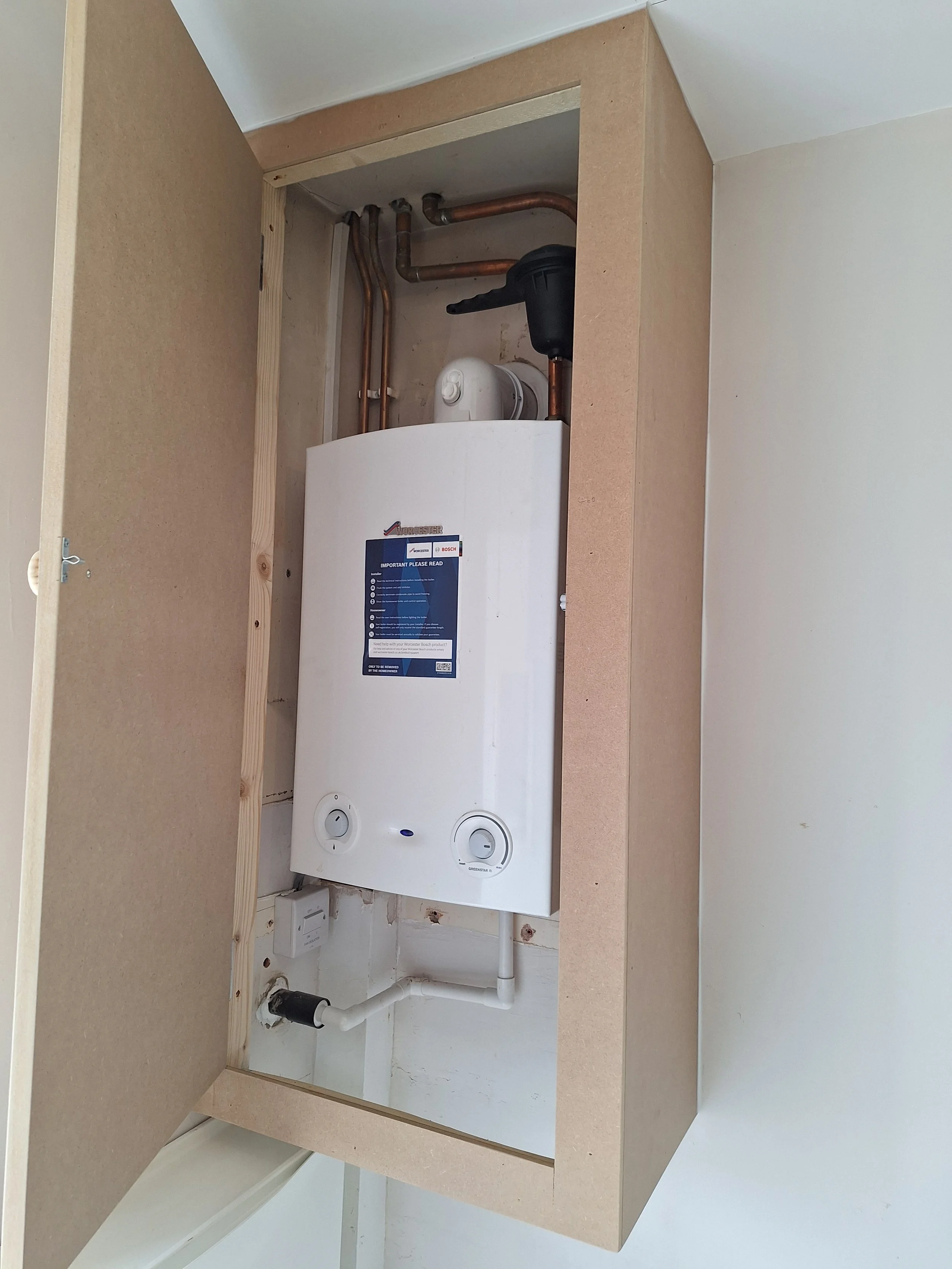Inside a built-in cabinet showing a water heater with pipes and control knobs.