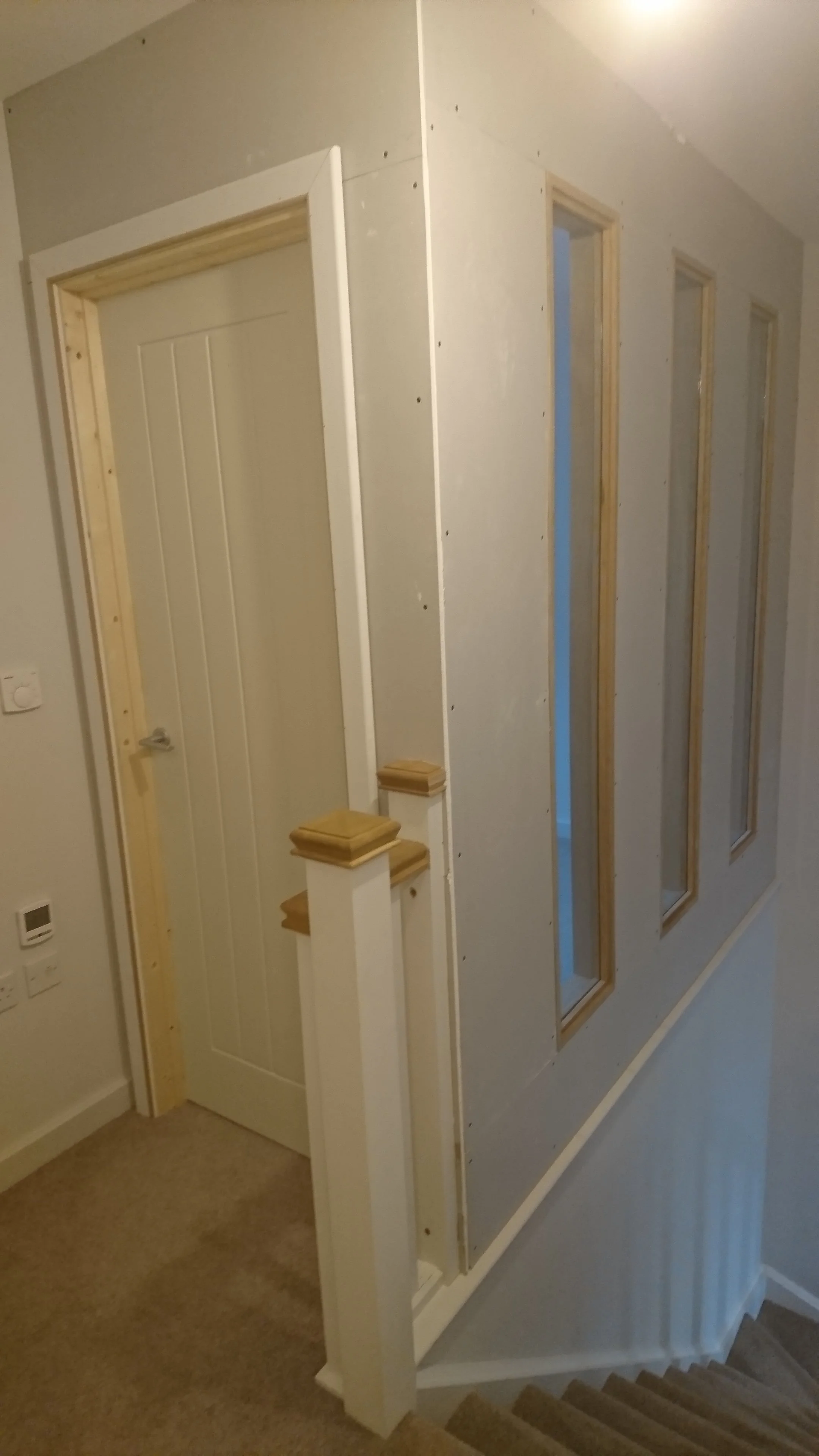 Partially constructed interior wall with three framed windows and a stairway with carpeted steps.