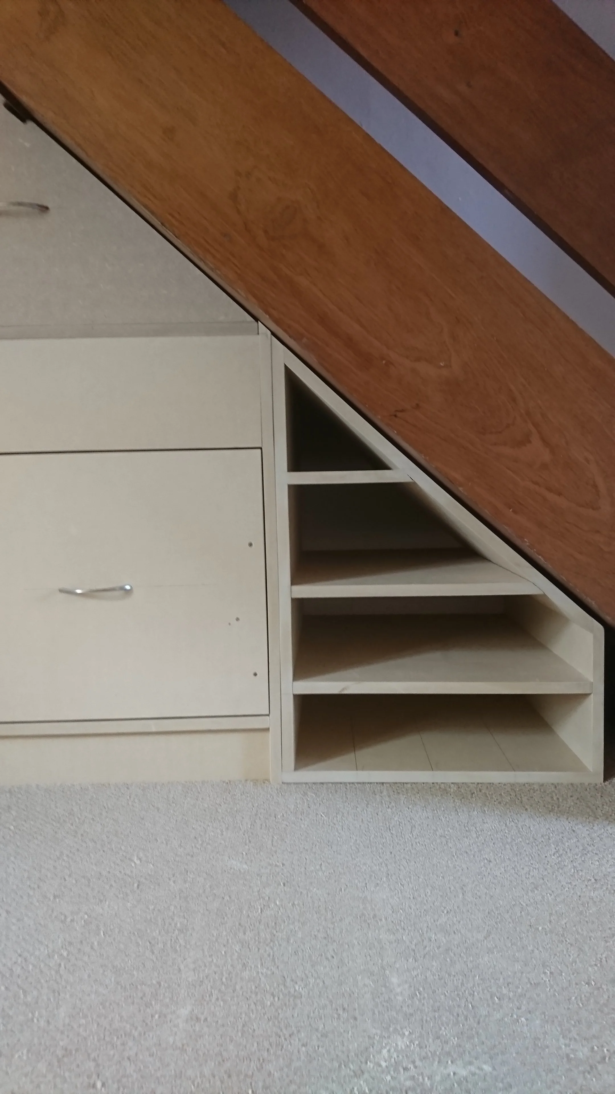 Part of a wooden desk and beige cabinet with shelves and drawers against a textured white wall.