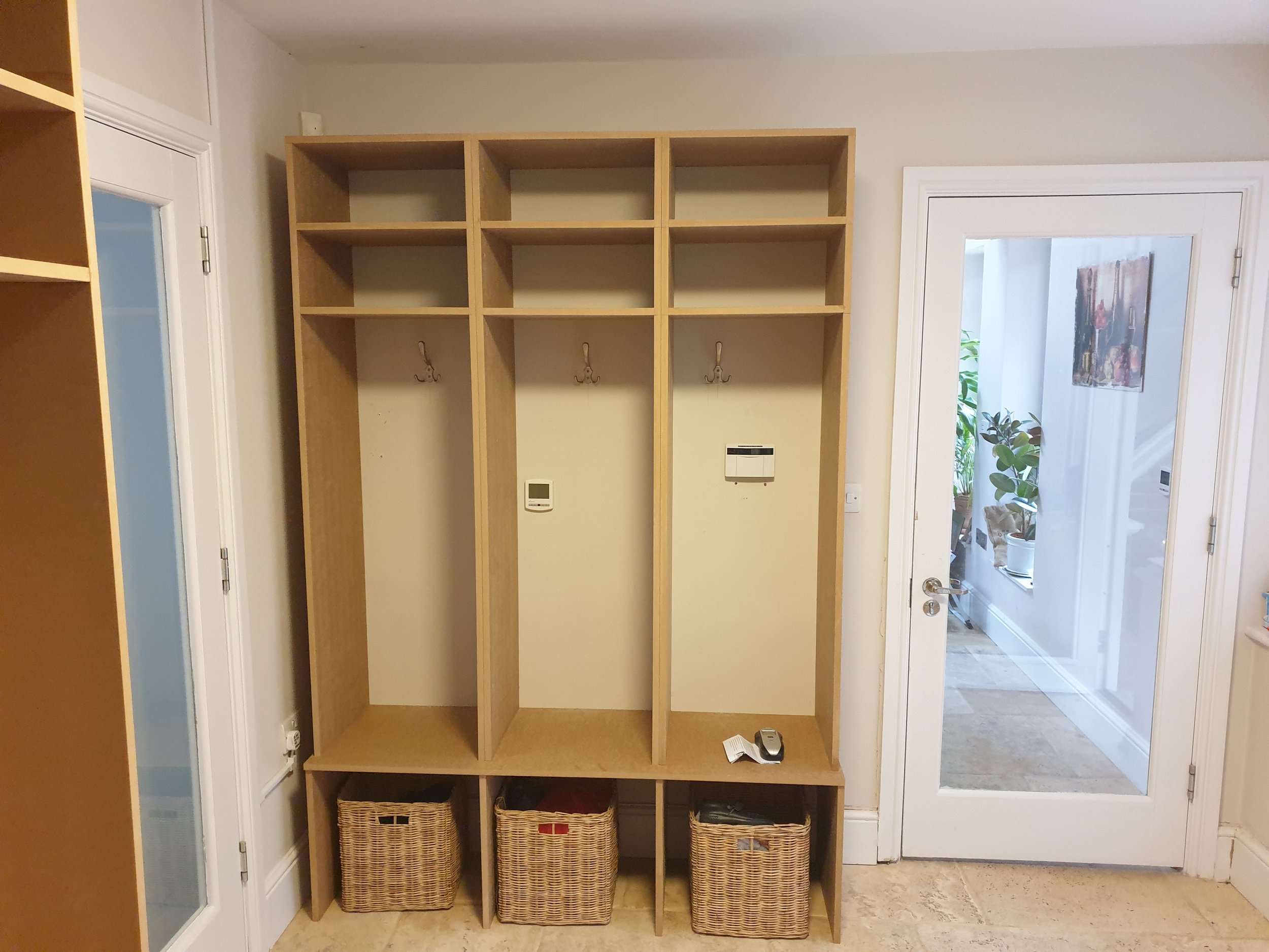 Wooden hall tree with hooks, shelves, baskets below, and a door with glass panel to the right, in a home interior.