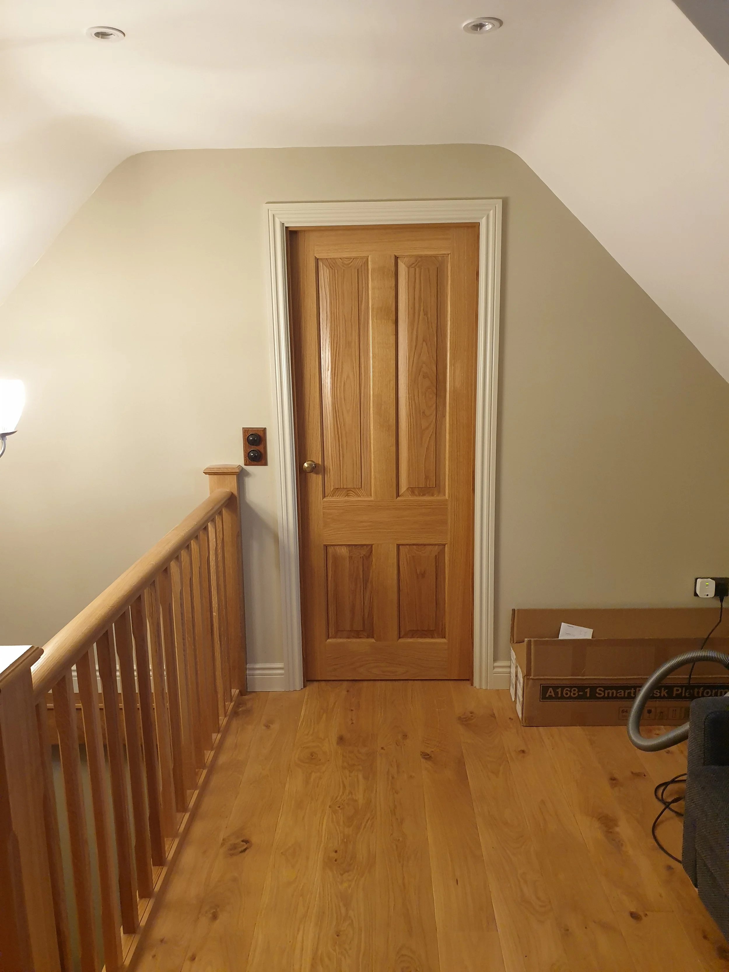 Wooden door at the top of a short staircase with a wooden railing on the left. There's a small box on the right side of the door and some electrical outlets on the wall.