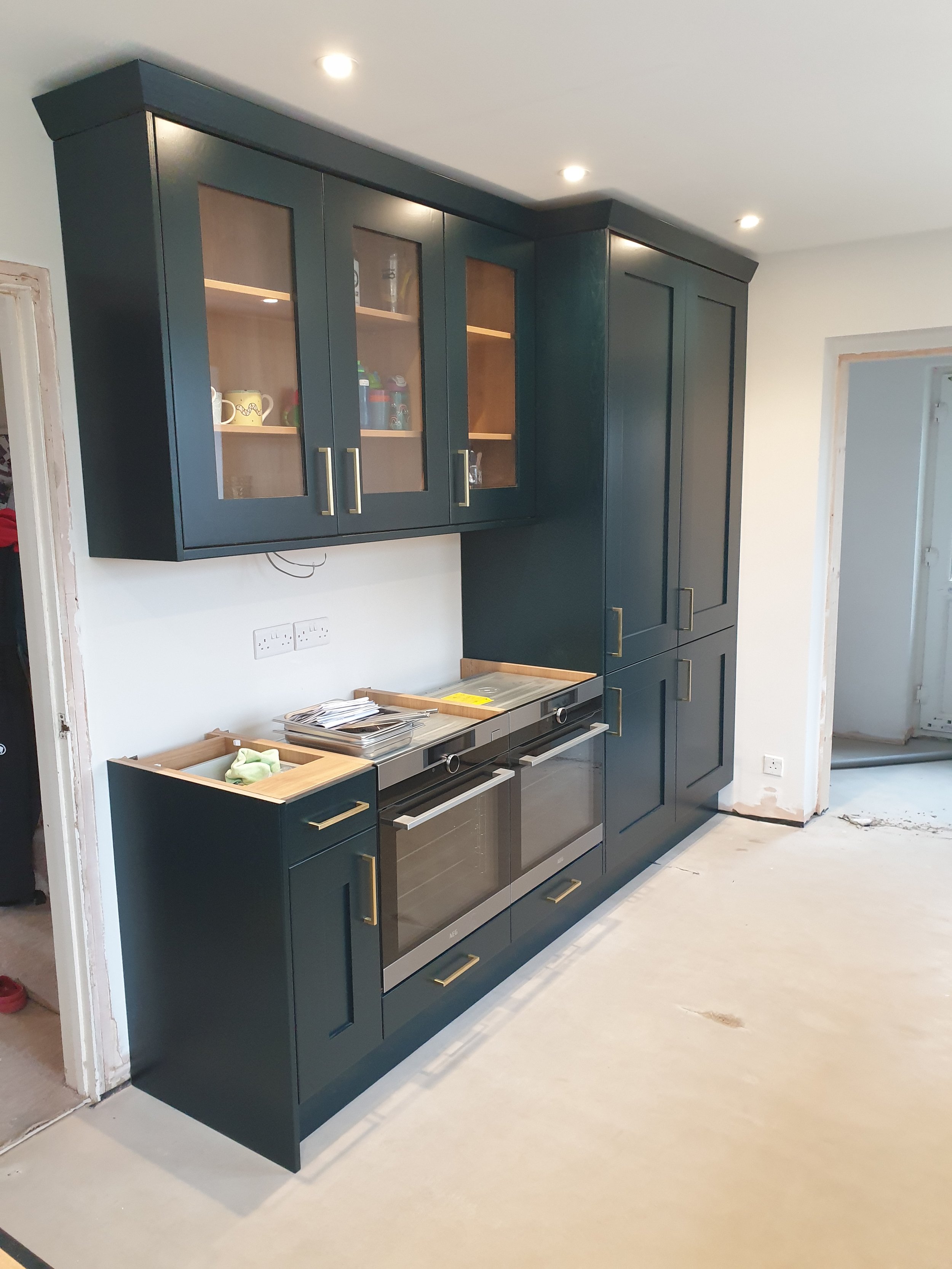 Kitchen with black cabinets, glass-front upper cabinets displaying cups and bottles, and a built-in oven and stove.