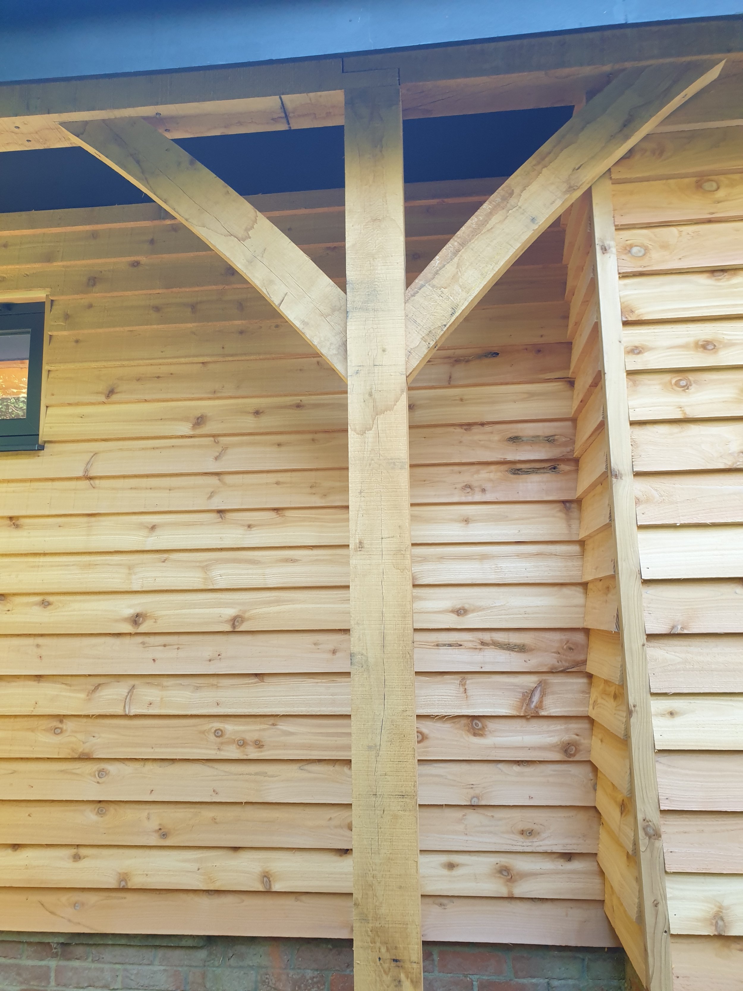 Close-up of a wooden structure supporting the roof of a building, with horizontal wooden siding and a small window visible on the left side.