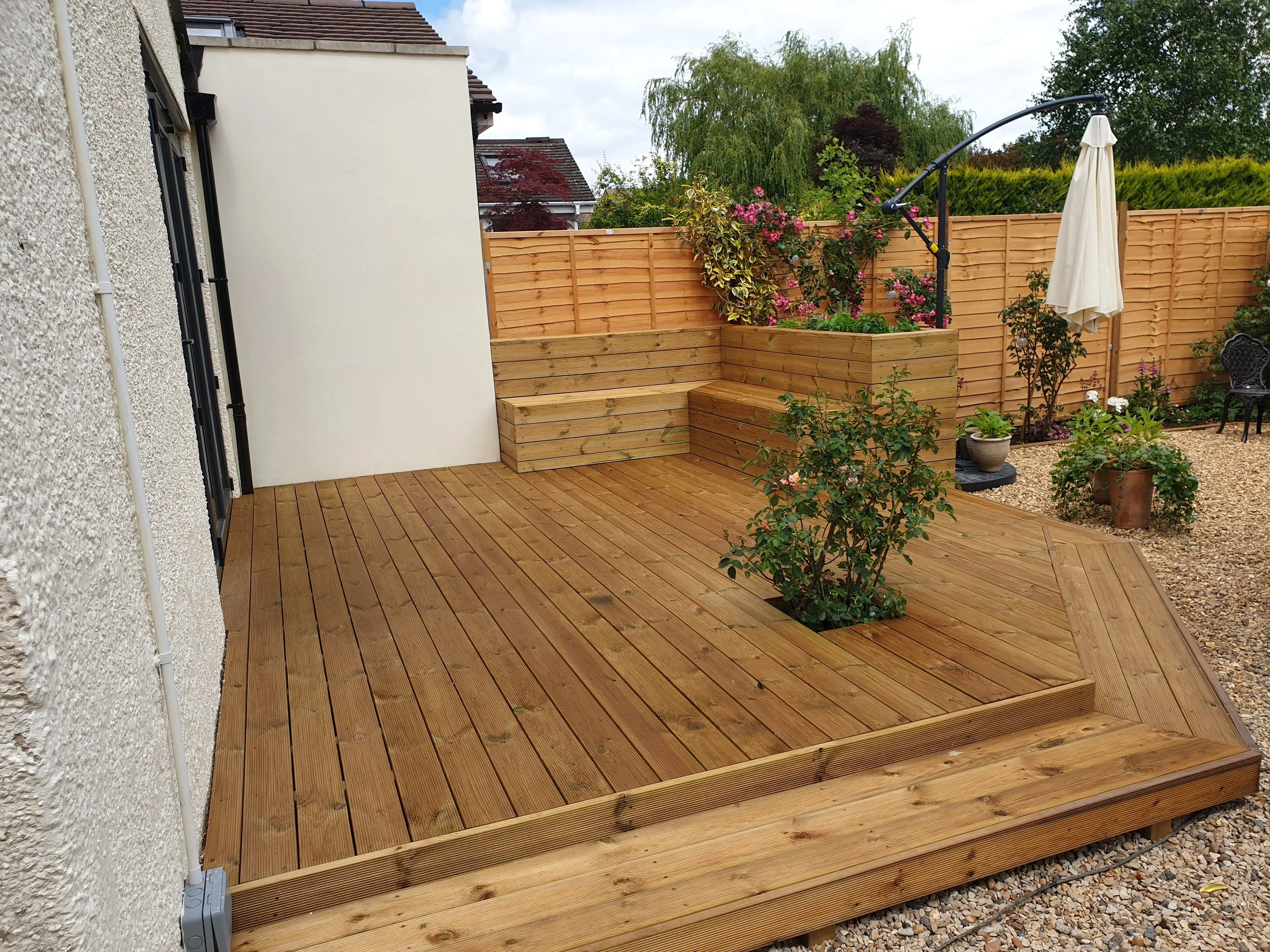 A newly constructed wooden deck with outdoor plants, a patio, and garden furniture in a backyard.