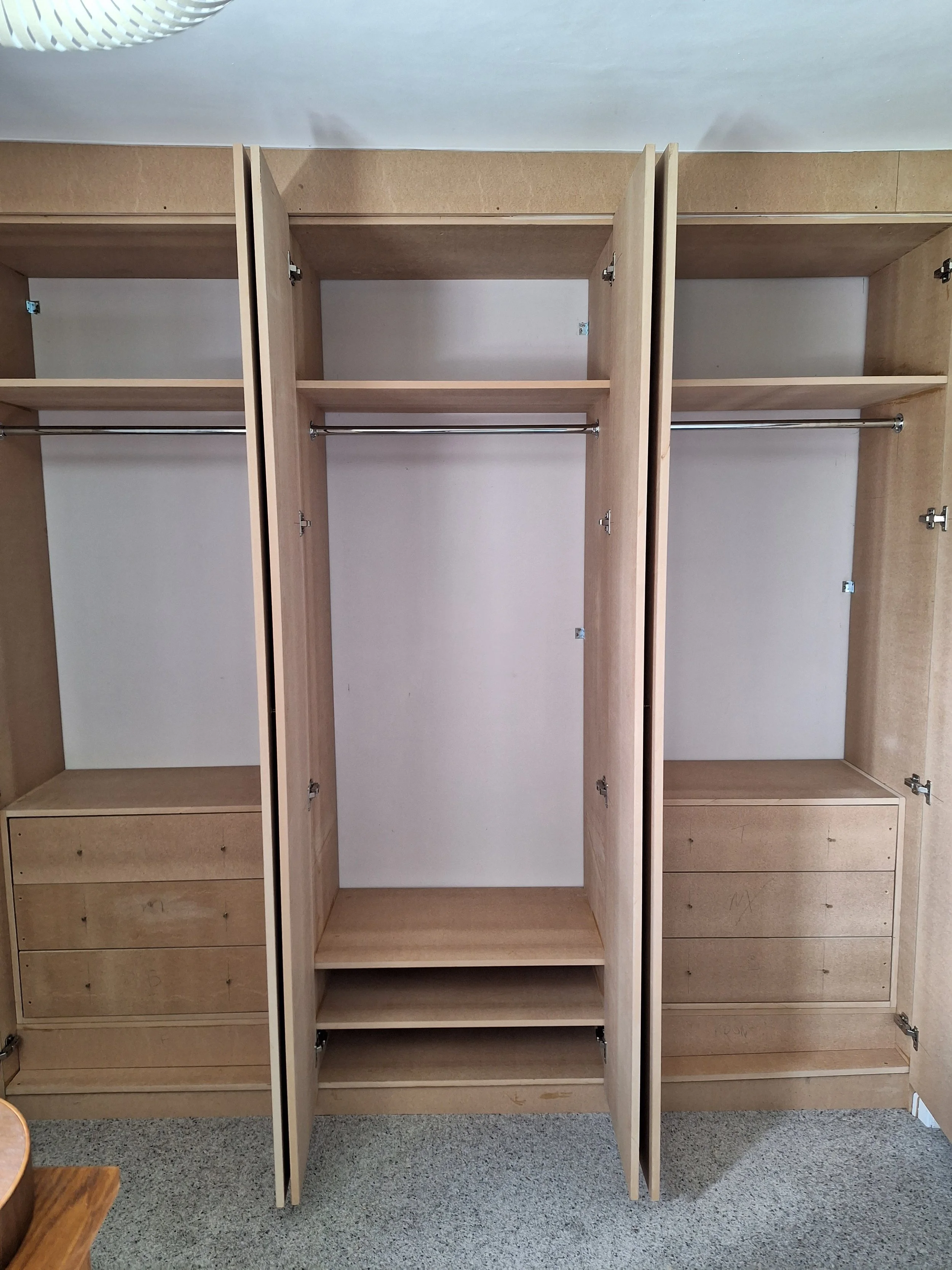 Empty wooden closet with open doors, hanging rods, shelves, and drawers inside.
