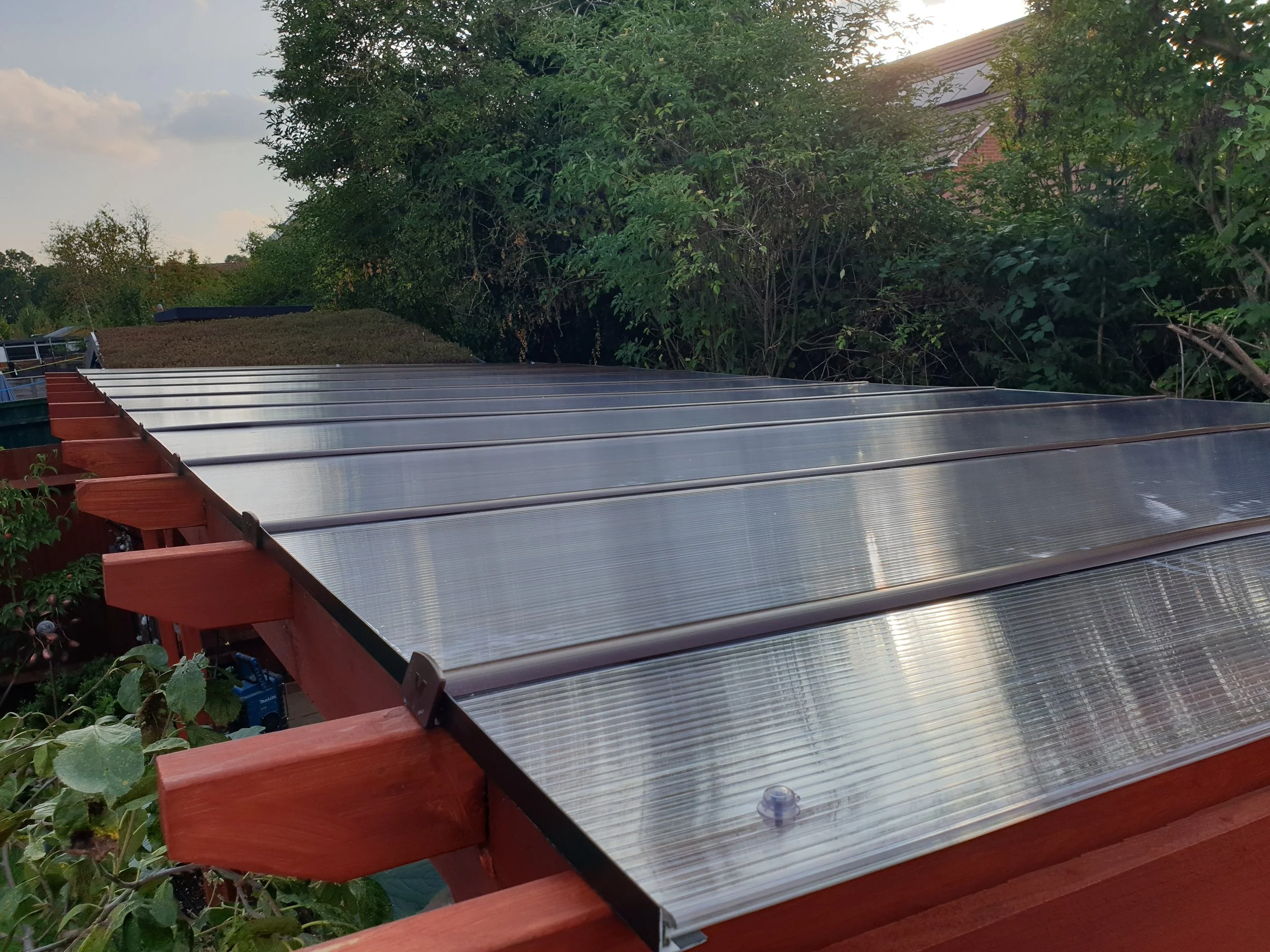 A set of solar panels installed on a wooden deck, with trees and a house in the background during the daytime.