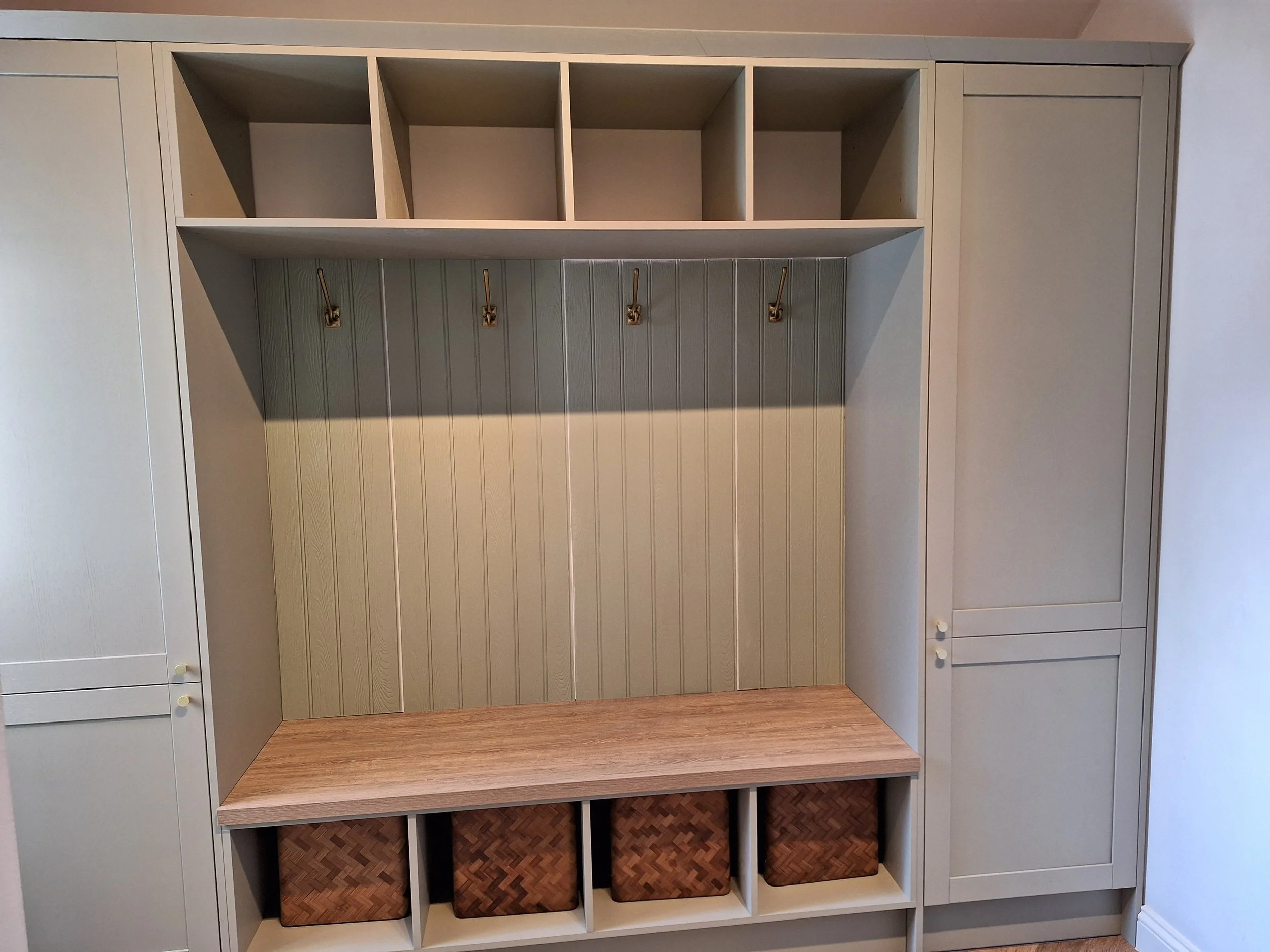 Built-in storage unit with cubbies, hooks, and baskets, with a wooden bench and storage compartments at the bottom.