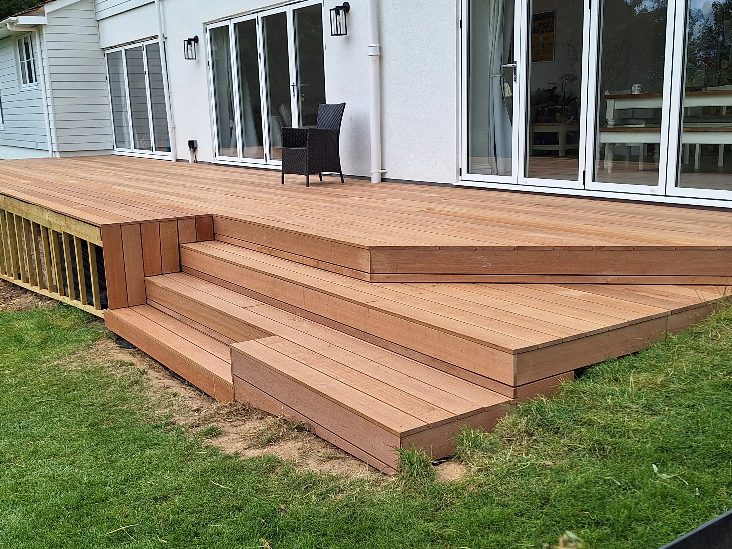 Wooden deck with stairs leading down to grass in backyard of house with glass sliding doors and patio furniture.