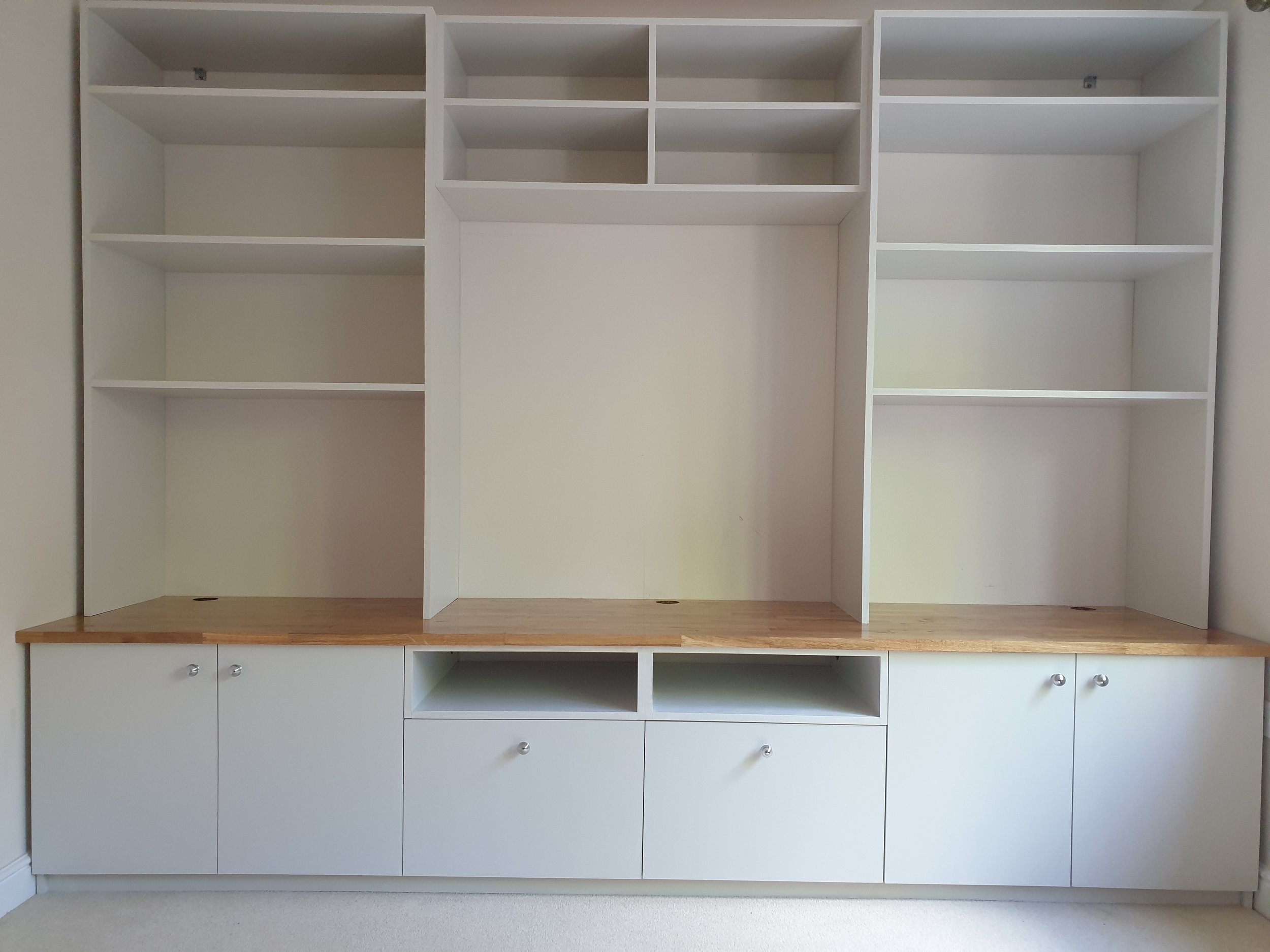 Empty built-in white shelving unit with wooden countertop and cabinet doors at the bottom.