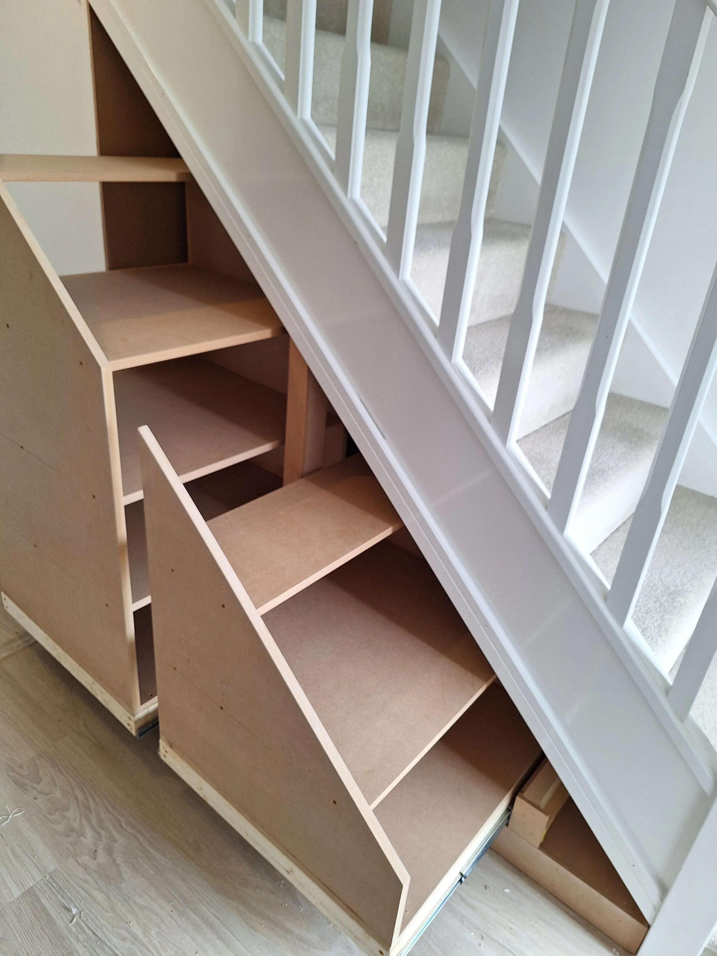 Partially assembled wooden staircase with built-in storage drawers beneath.