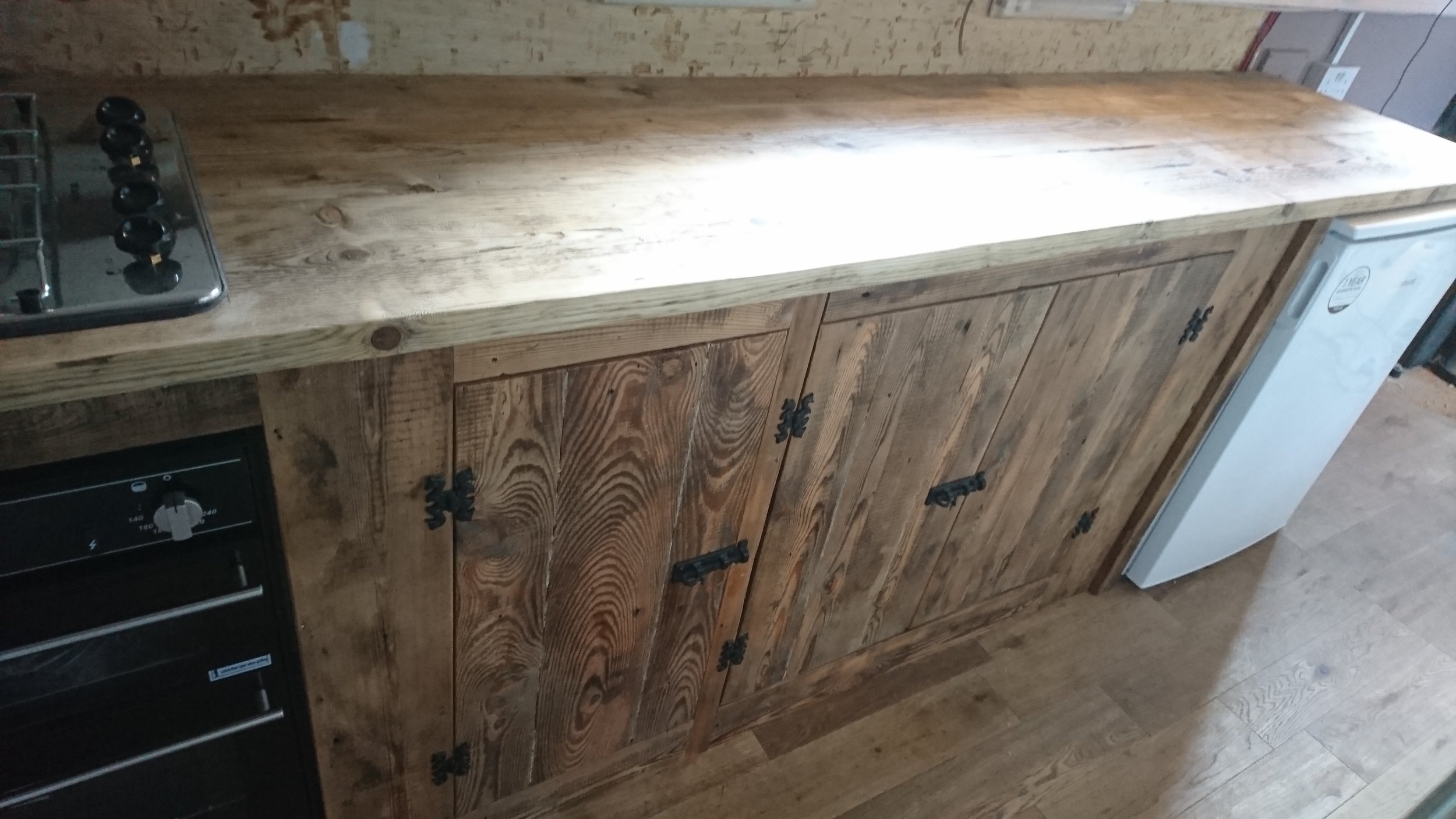 Rustic kitchen counter made of stained wood with a gas stove on the left and a white small appliance on the right, with cabinets below.