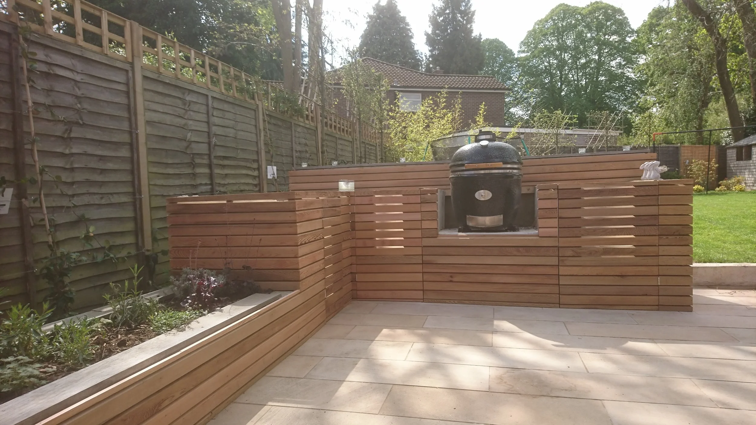 Modern backyard patio with wooden privacy screens, built-in planter, and a black kettle-style barbecue grill.