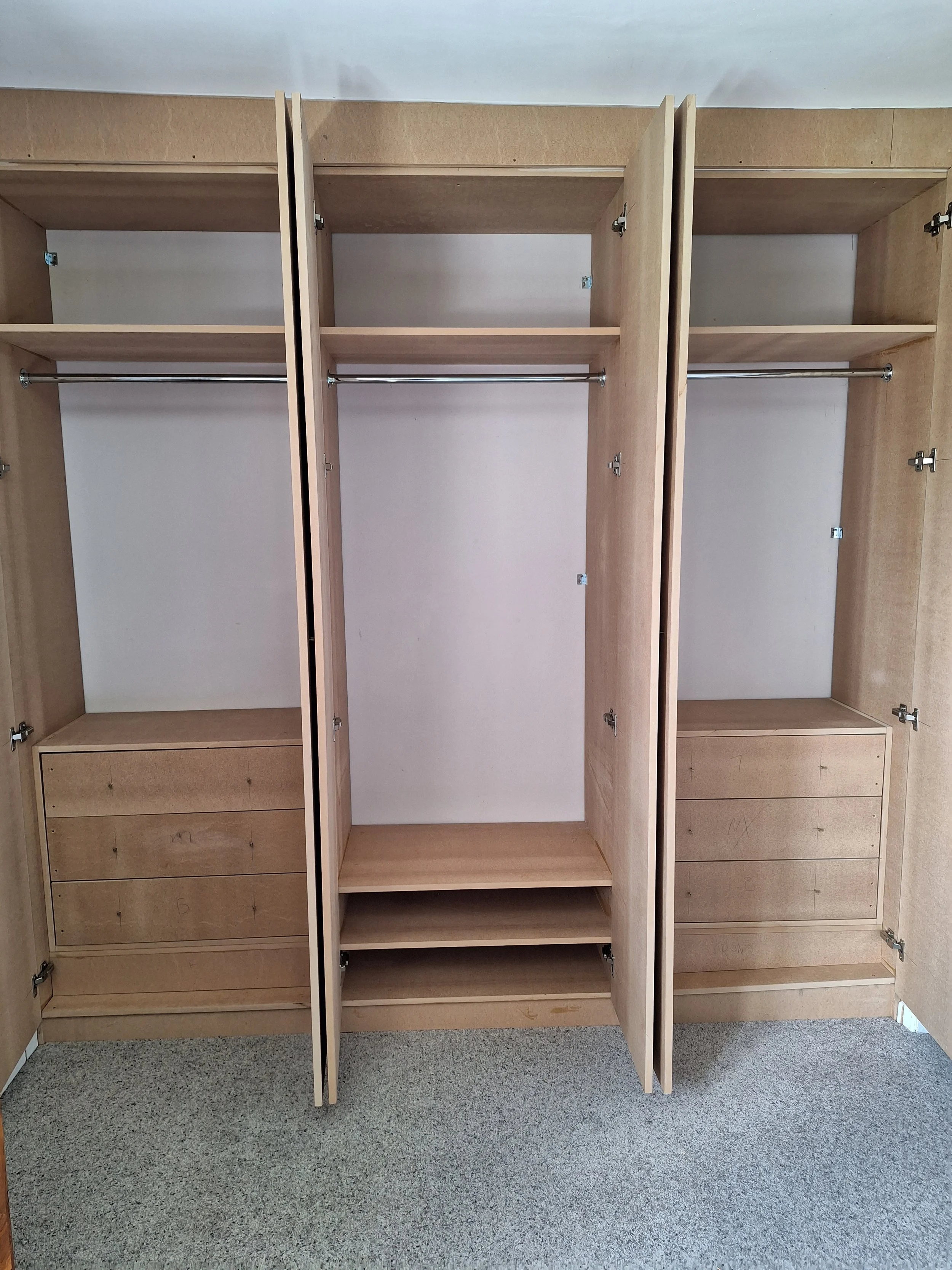 Empty wooden closet with open doors, featuring shelves, drawers, and hanging rods.