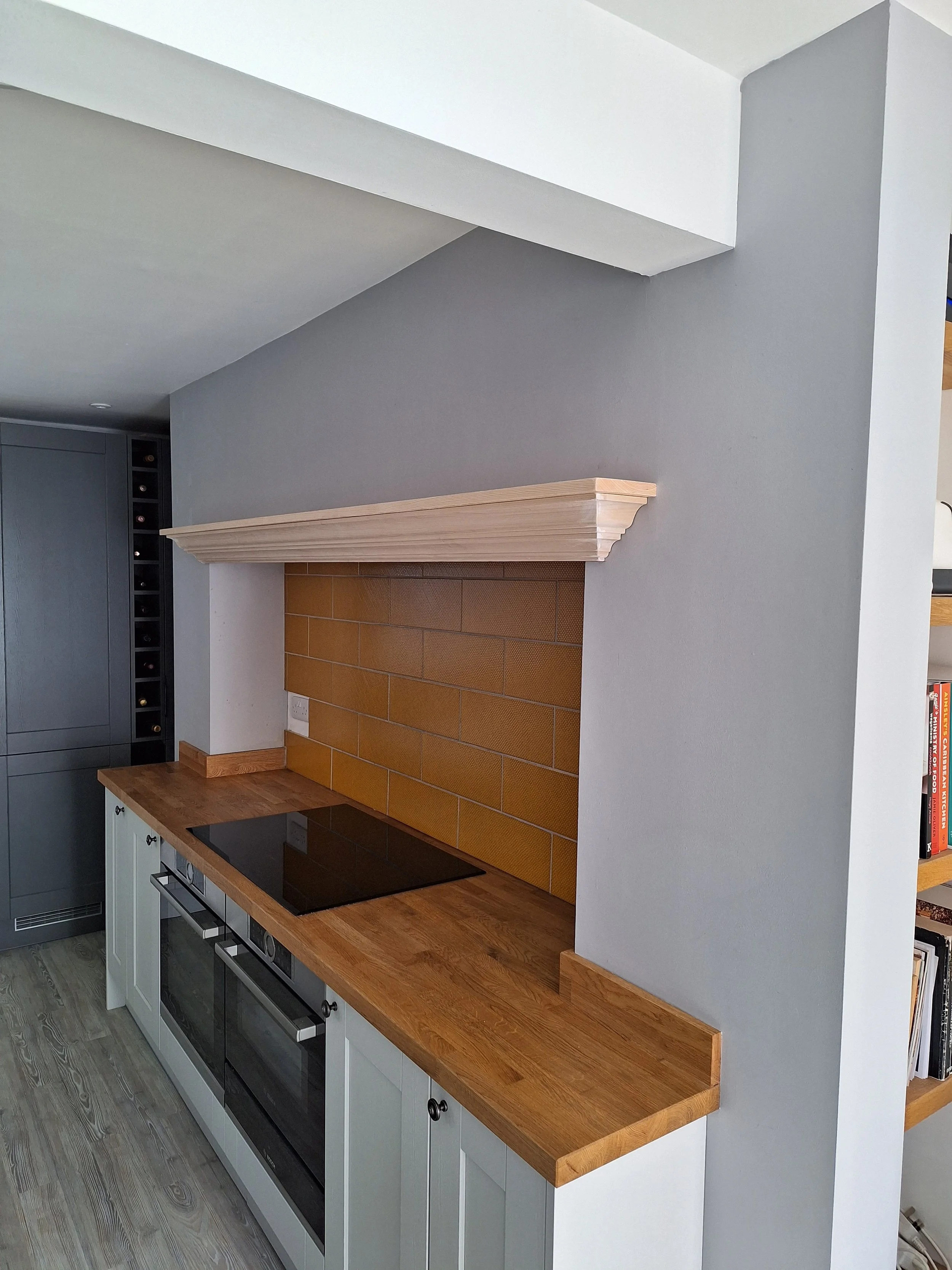 A modern kitchen with a gray wall, a wooden countertop, and a decorative white mantle above a brick backsplash.