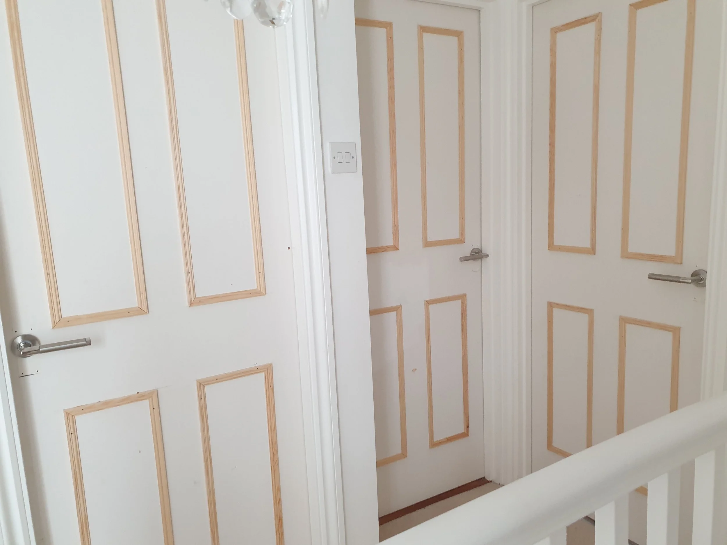 Interior view of white doors with decorative wooden paneling and metal door handles, part of a hallway or room.