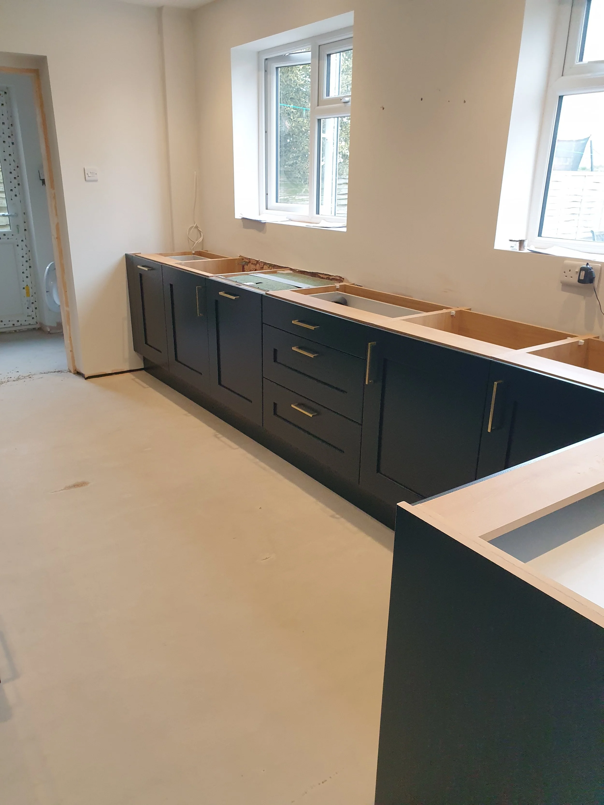 Kitchen under construction with dark cabinets and window above the countertop, which is unfinished.