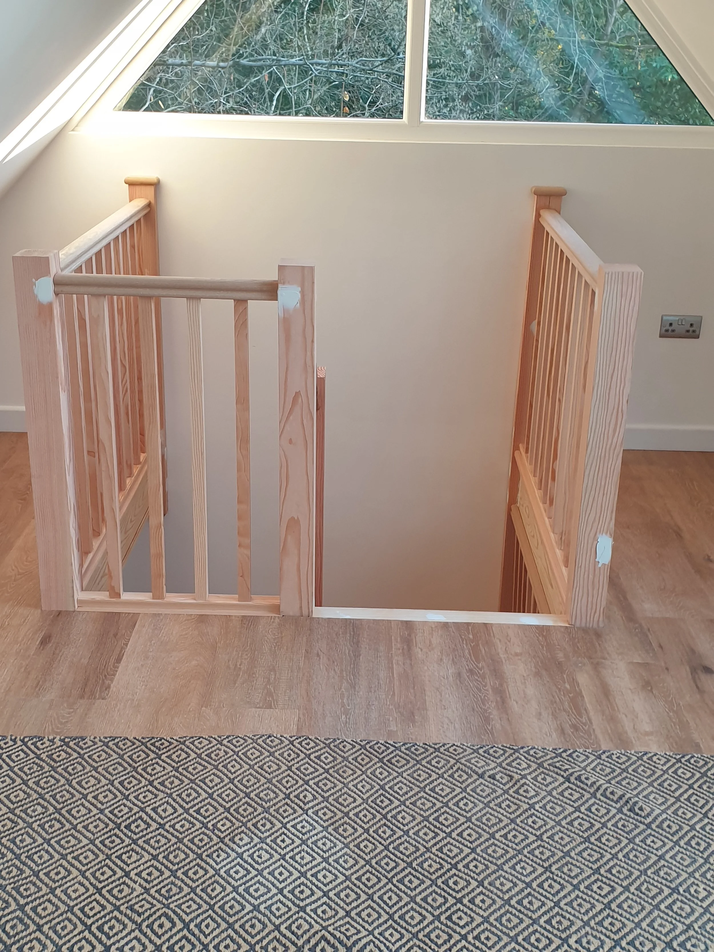 Unfinished wooden staircase with railings leading down from a skylight window, located in a room with beige walls and hardwood flooring.