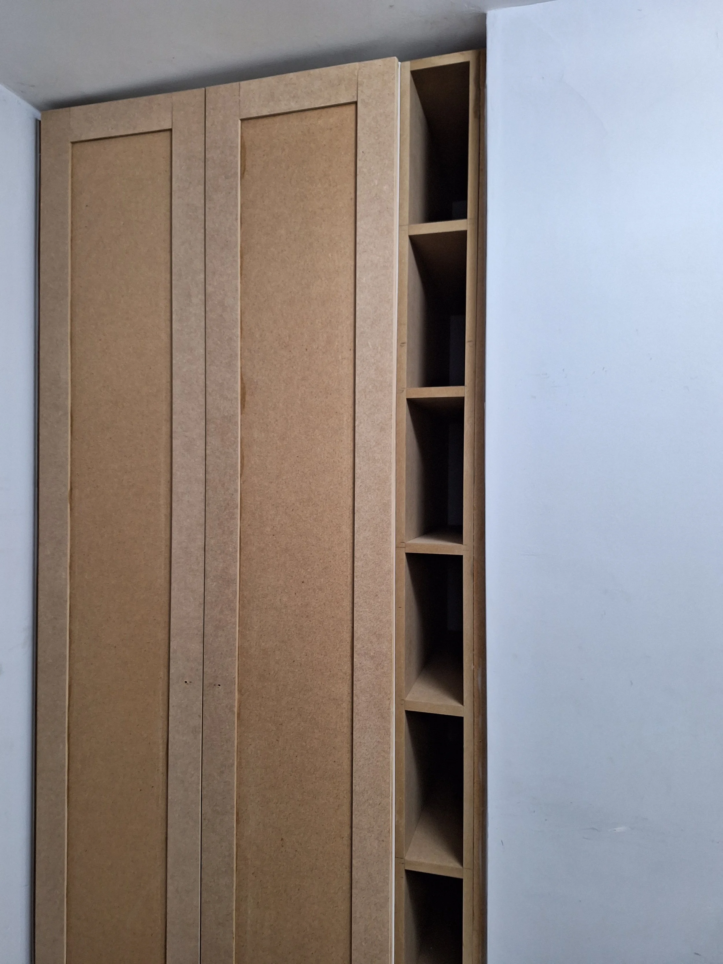 Wooden panel with built-in open cubbies on a wall in a room under construction or renovation.
