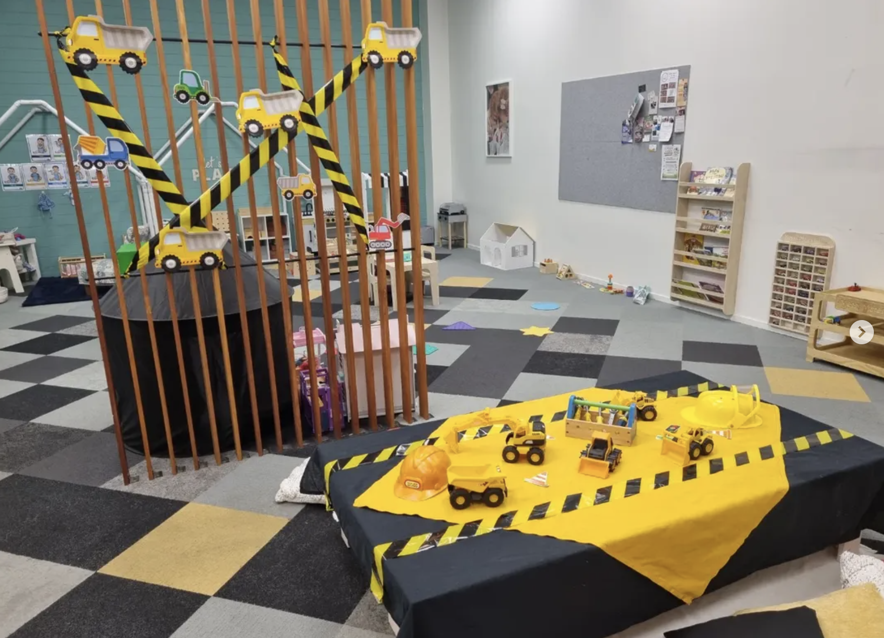 Children's indoor play area with toy construction vehicles, safety barriers, and play equipment.