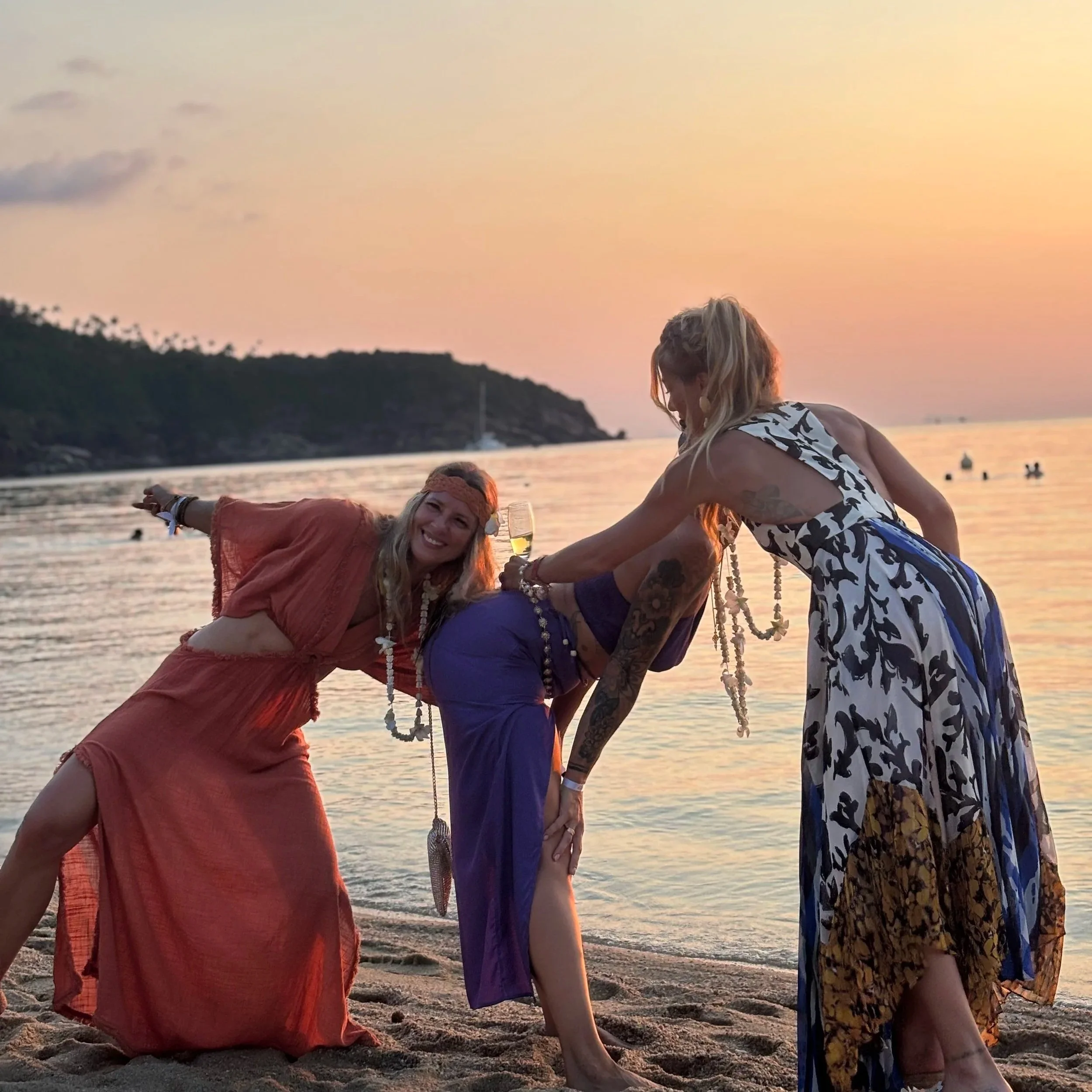 Two women laughing and dancing together at sunset on the beach during Sirius Wild Woman Retreat, Koh Phangan