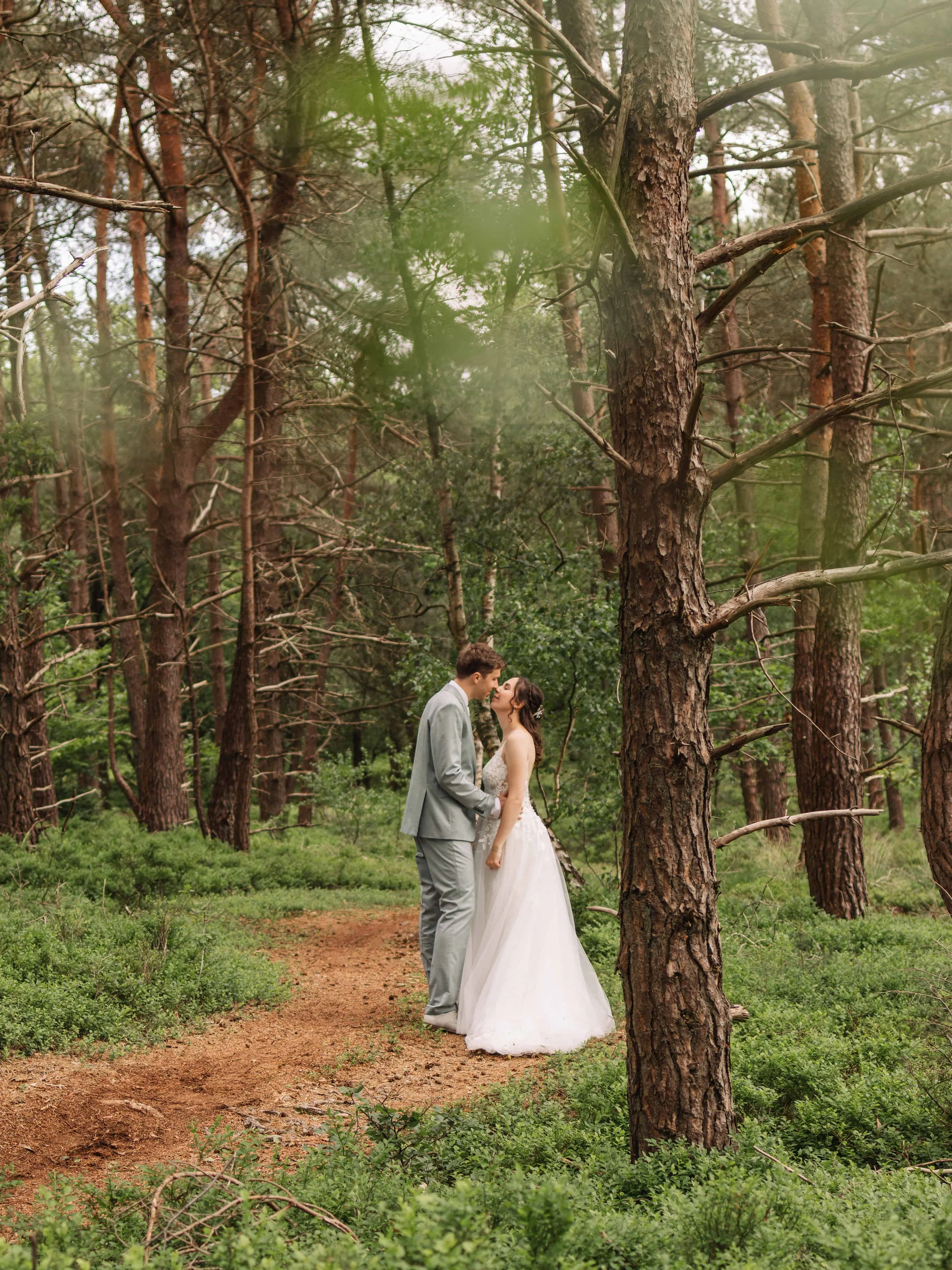 Een bruid en bruidegom staan in een bos, ze kijken elkaar liefdevol aan tijdens hun huwelijksfotografie.