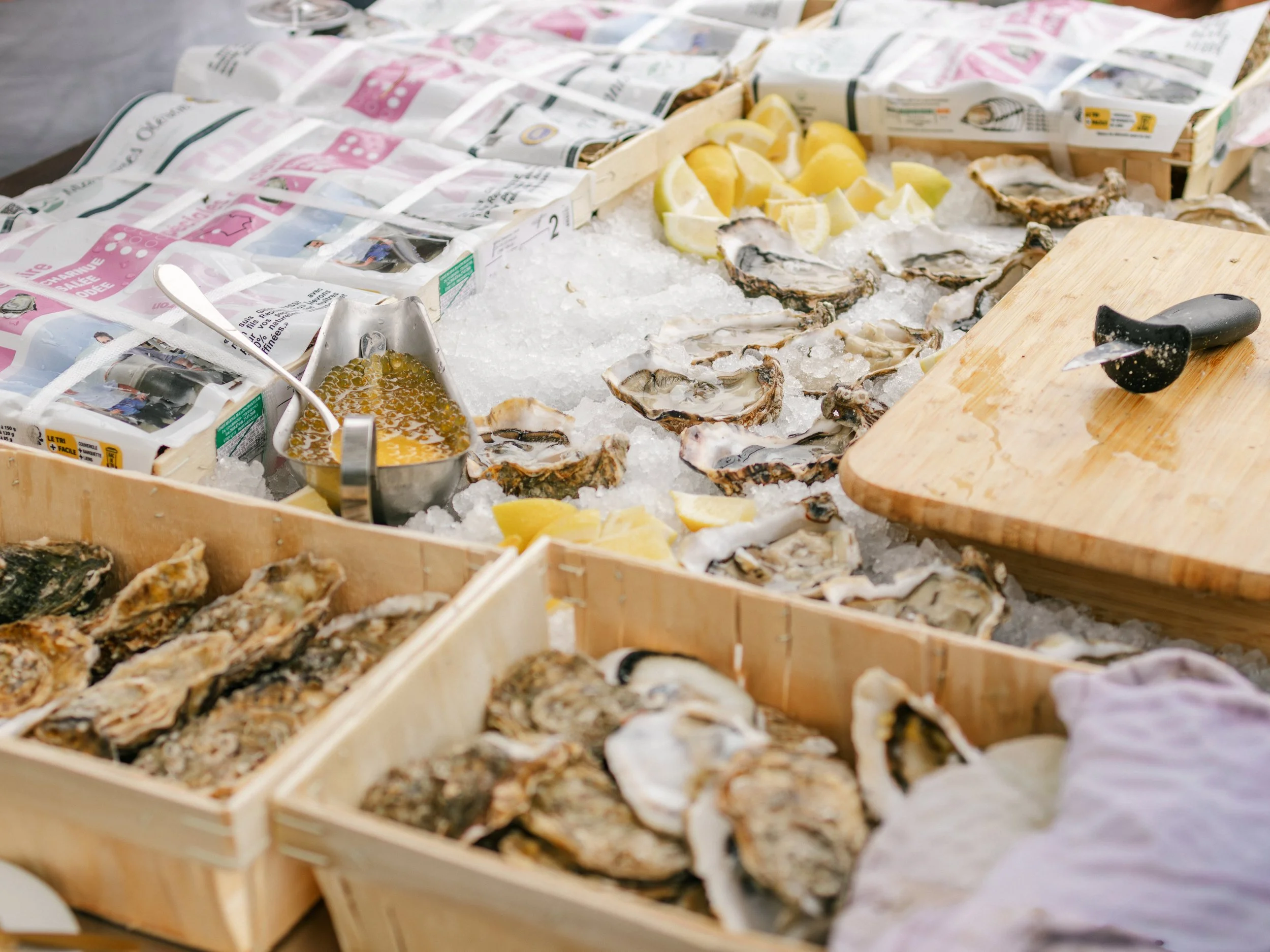 Verse oesters en citroenparten op een bed van ijs, met een snijplank en een schaal met oesters.