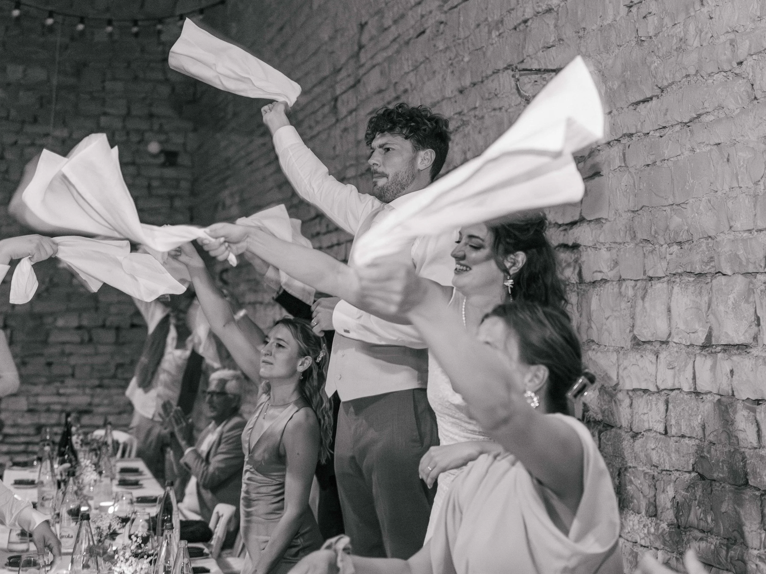 Mensen die meezingen en dansen met servetten tijdens een feest of viering, binnen bij een stenen muur.