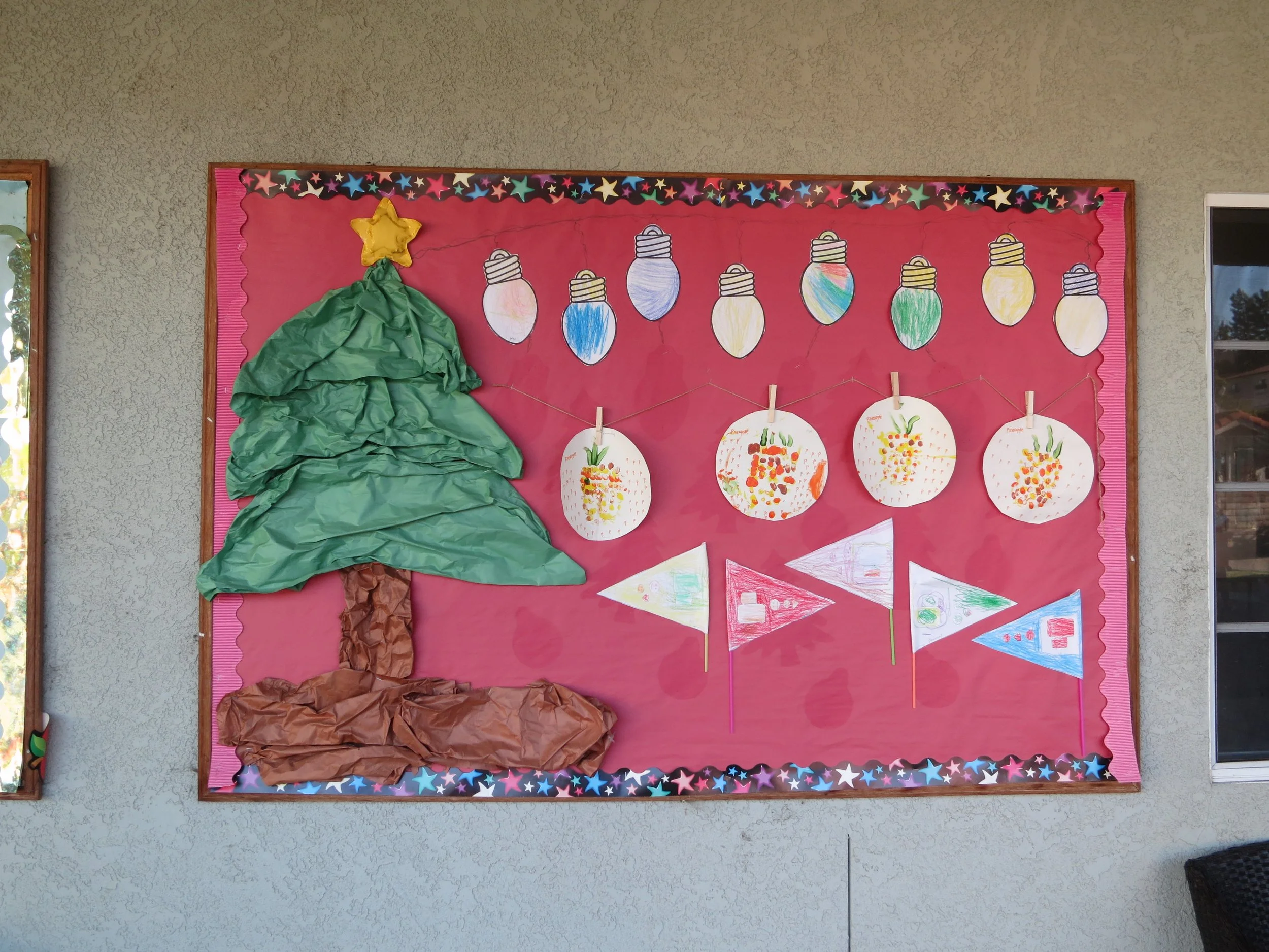 Decorative Christmas bulletin board with a crumpled green paper Christmas tree, topped with a yellow star, set against a red background with hand-drawn ornaments and banners. (The Cross Schools of Education - Walnut, CA)