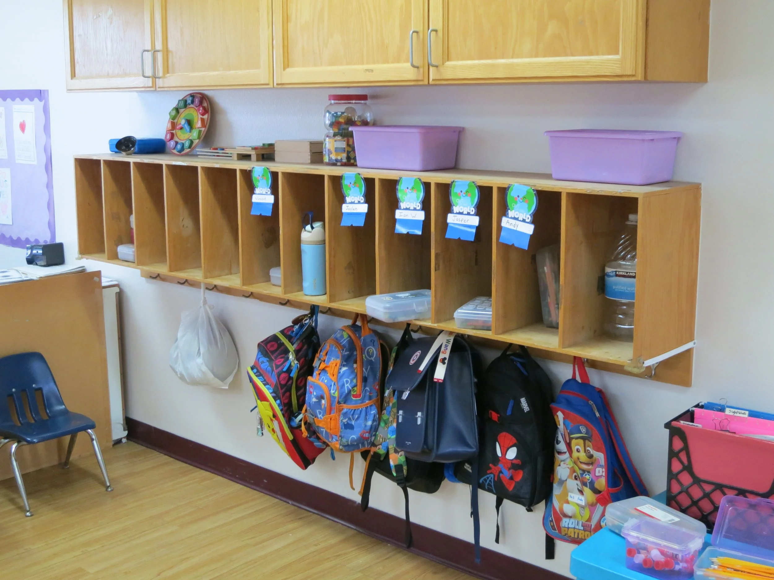 Preschool classroom cubbies with backpacks and hooks, and shelves with various classroom supplies. (The Cross Schools of Education - Walnut, CA)